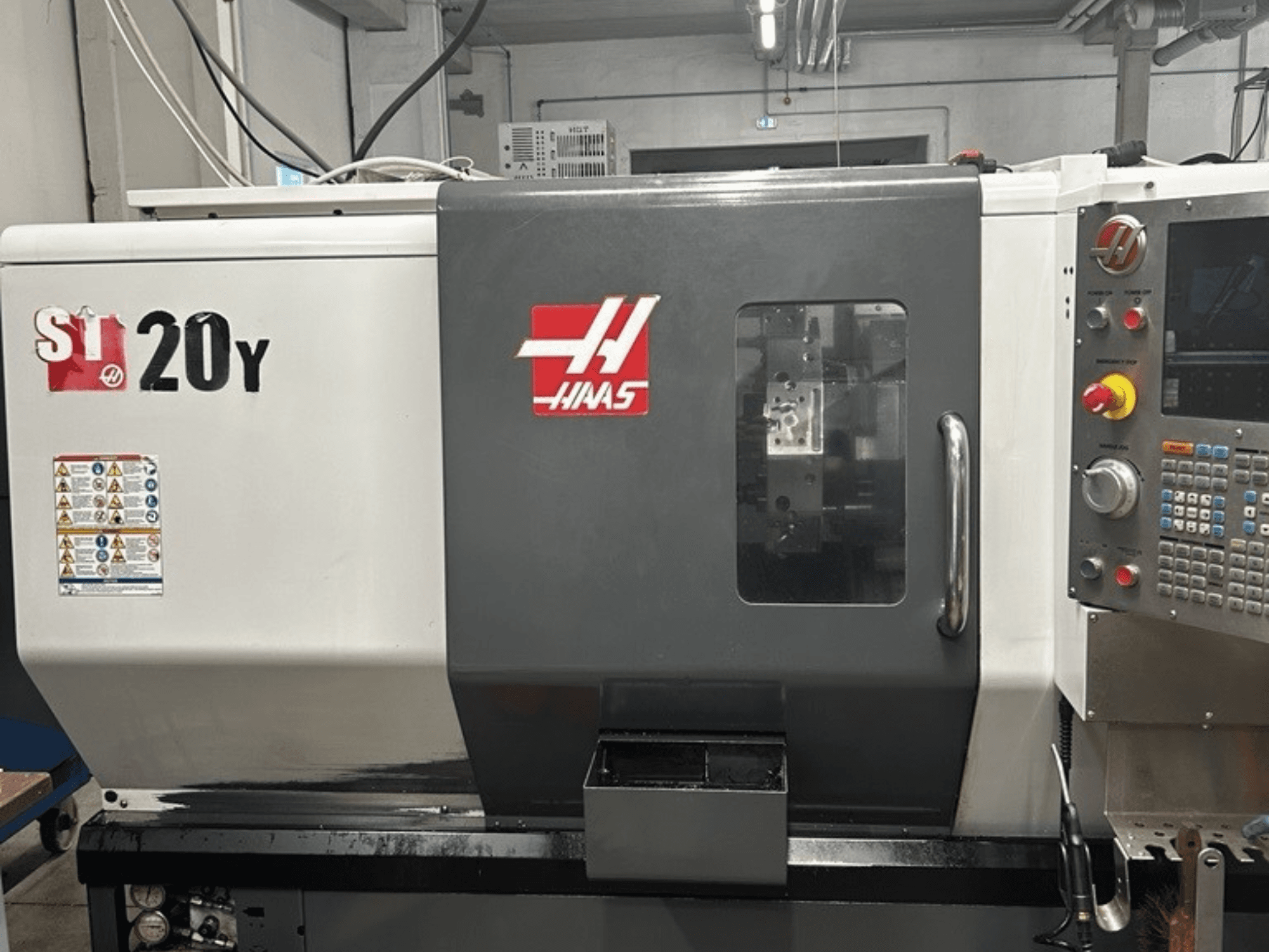 Torno CNC Haas ST-20Y, vista frontal, mostrando el panel de control, las etiquetas de seguridad y la ventana operativa.