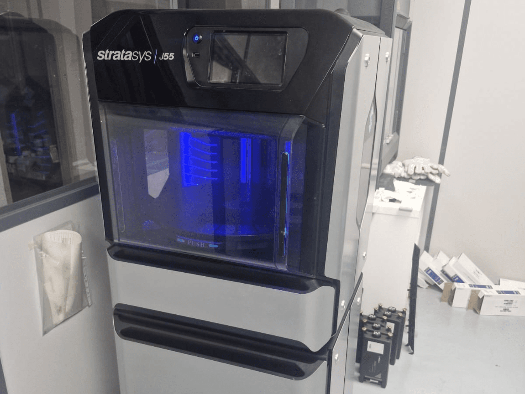 Impresora 3D de plástico Stratasys J55 Prime en una vista lateral, mostrando su elegante diseño y el área de impresión iluminada.