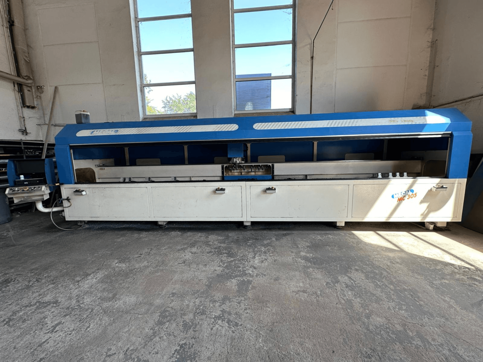 Vista frontal del centro de mecanizado vertical MECAL MC 305, con un diseño en azul y blanco, mesa de trabajo visible y panel de control.