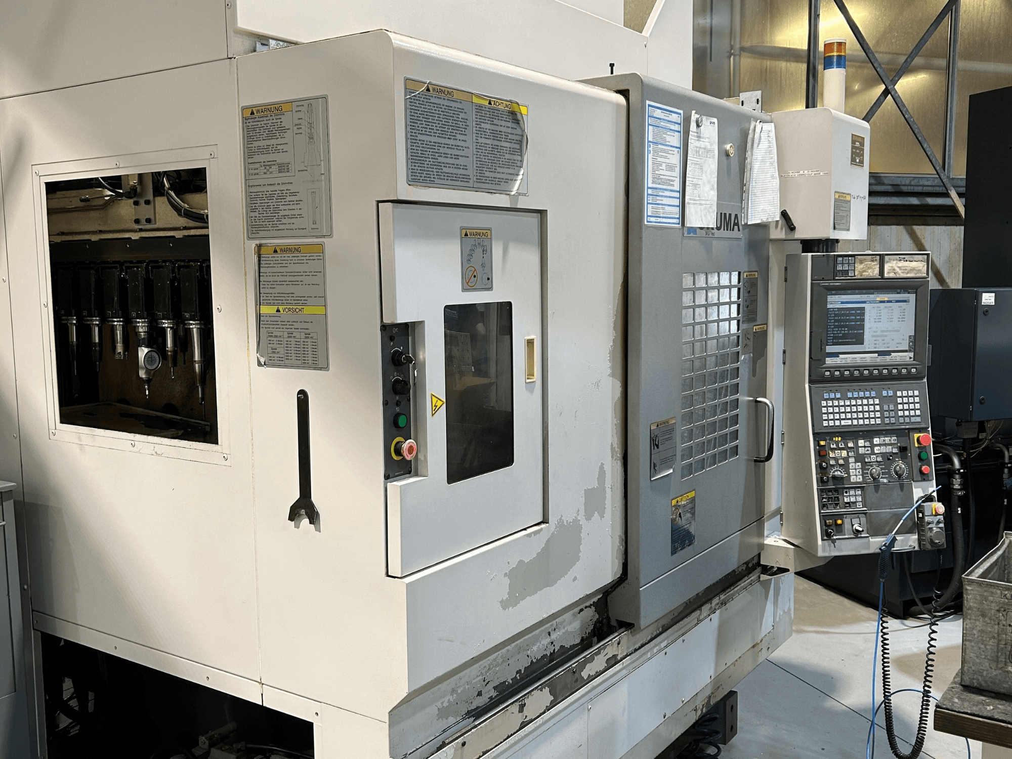 Vista frontal de una máquina CNC UMA con portaherramientas visibles, panel de control, etiquetas de advertencia y botones de funcionamiento.