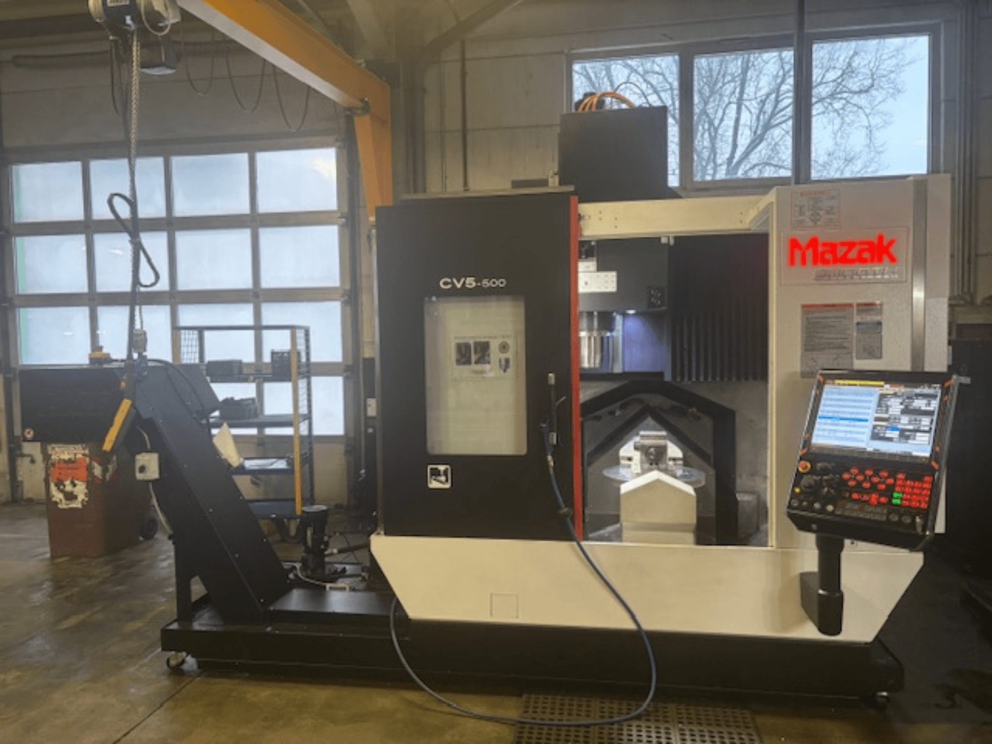 Mazak CV5-500 vertical machining center, front view, showcasing control panel, machining area, and overhead hoist.