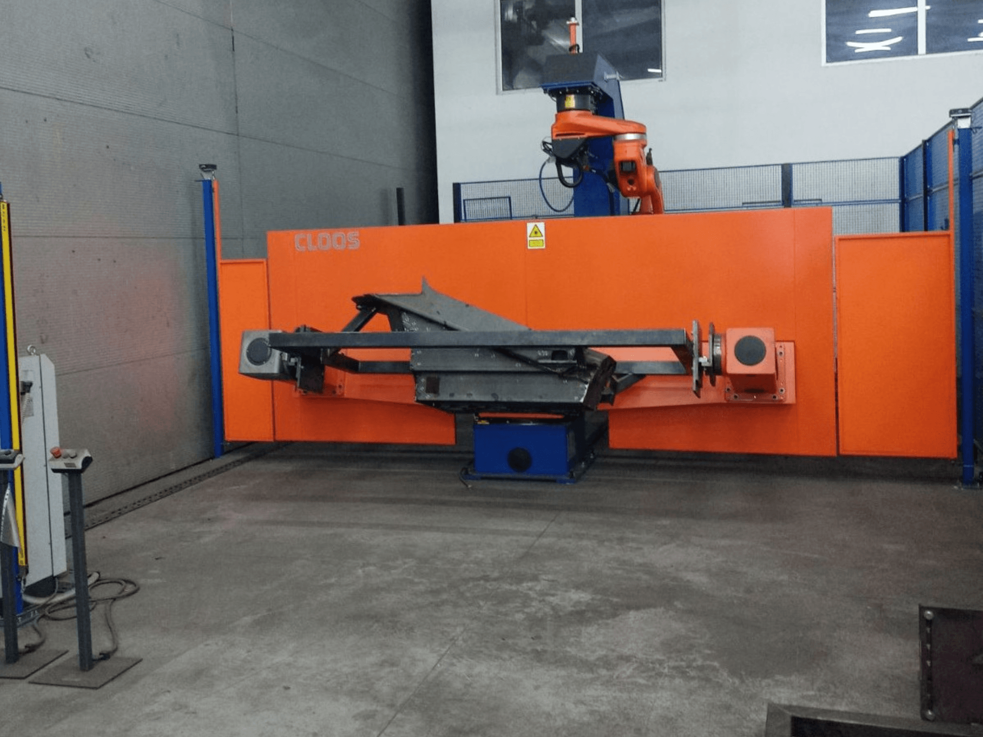 Vista frontal del sistema de automatización CLOOS QIROX QRC-350-E con brazo robotizado y estructura metálica en un entorno industrial.