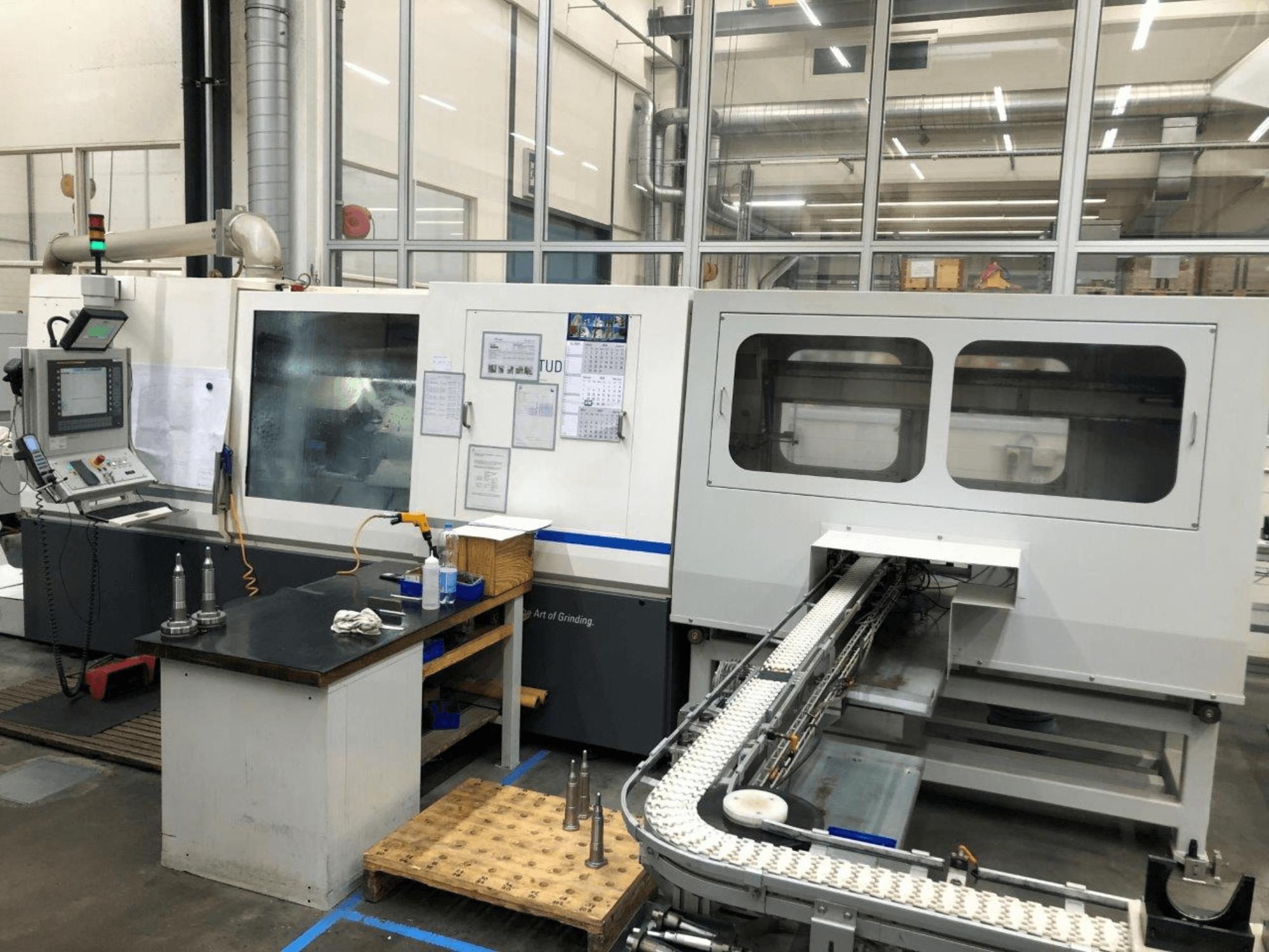 Rectificadora CNC con panel de control, vista frontal; cuenta con un transportador y ventanas de visualización claras, que muestran las herramientas de precisión.