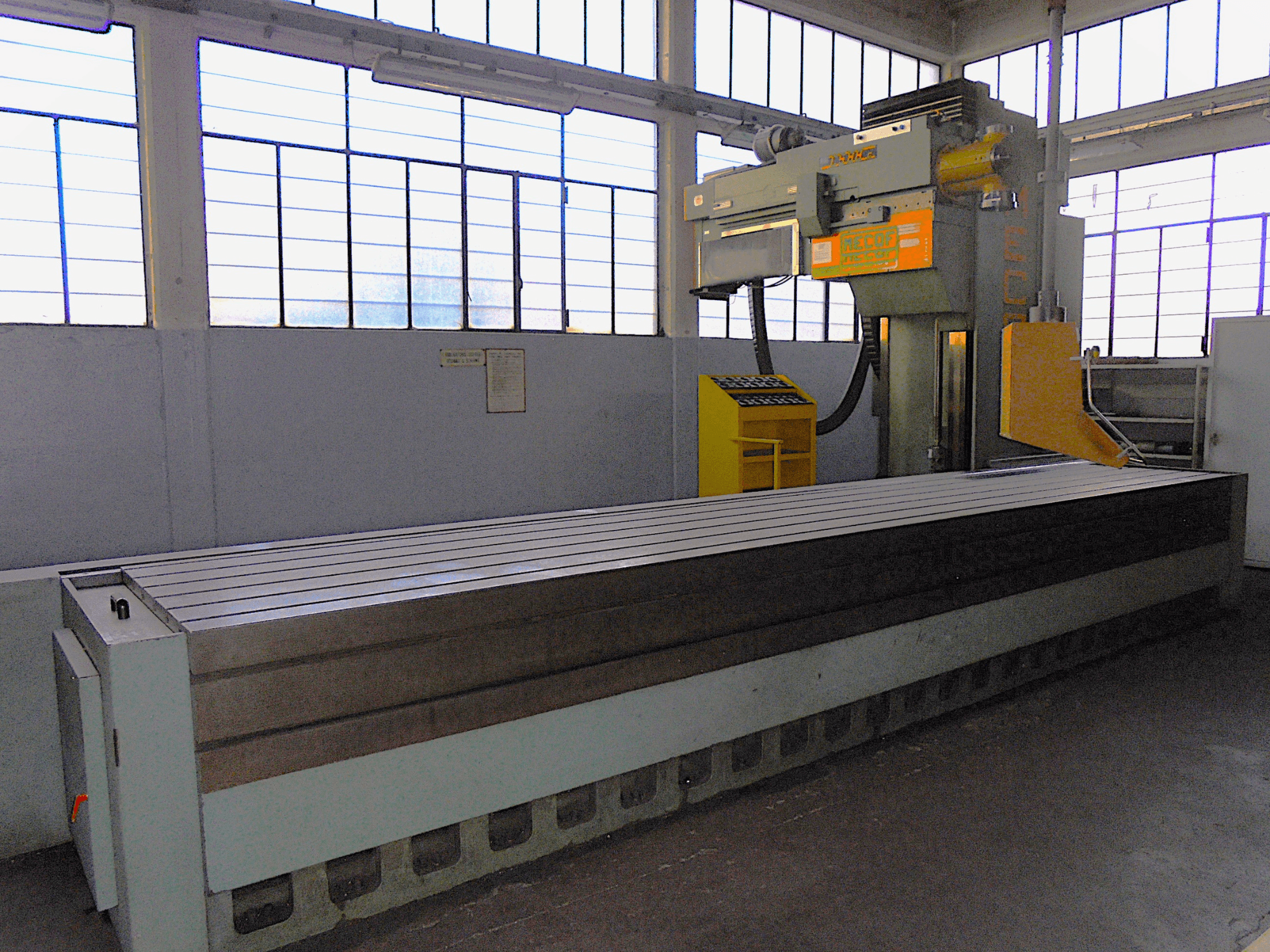 Marca desconocida, fresadora vertical en una fábrica, vista lateral, presenta una gran mesa con superficie acanalada y panel de control.