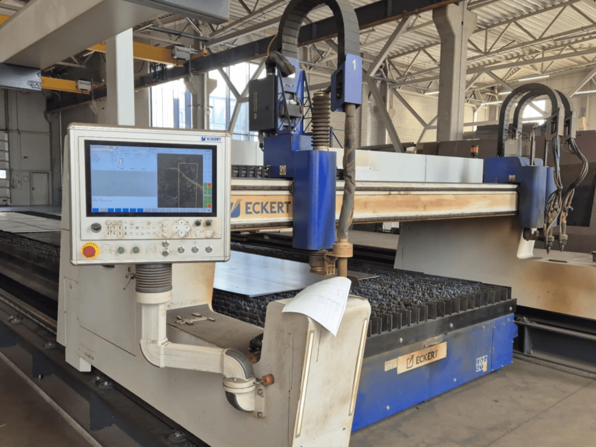 Panel de control de la máquina de corte CNC ECKERT en vista frontal, con una pantalla táctil y varios botones operativos.