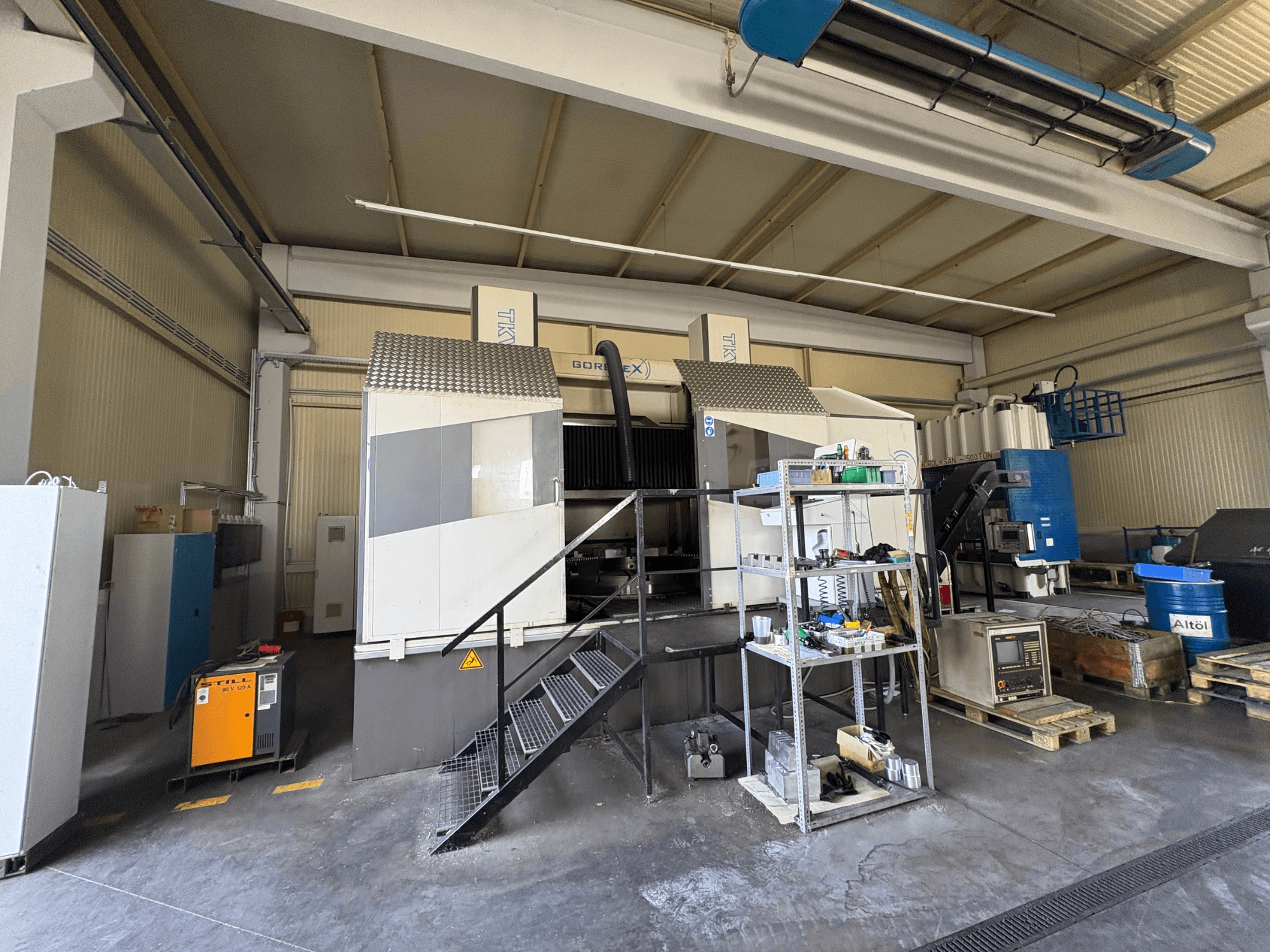 Configuración de mecanizado industrial con máquina GORAT X, vista lateral; incluye herramientas, panel de control y equipos en estanterías.