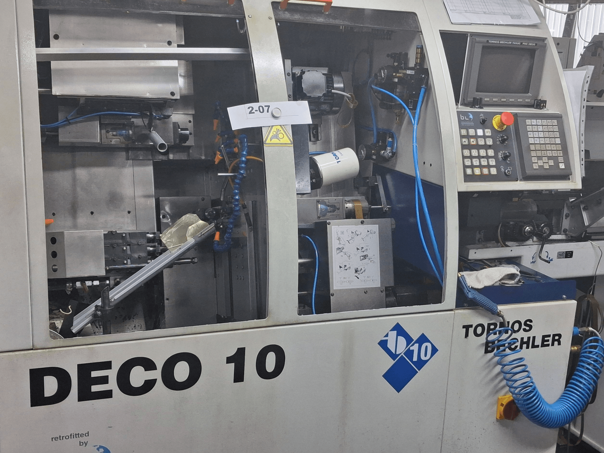 Vista en primer plano de la máquina de torneado TORNOS Deco 10a de tipo suizo, mostrando el mecanismo interno y los detalles del panel de control.