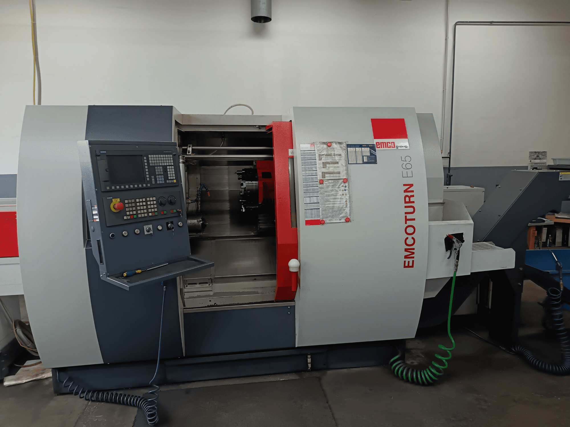 Centro de torneado y fresado EMCO EMCOTURN E65, vista frontal que muestra el panel de control, el mecanismo interno y las características en un entorno de taller.