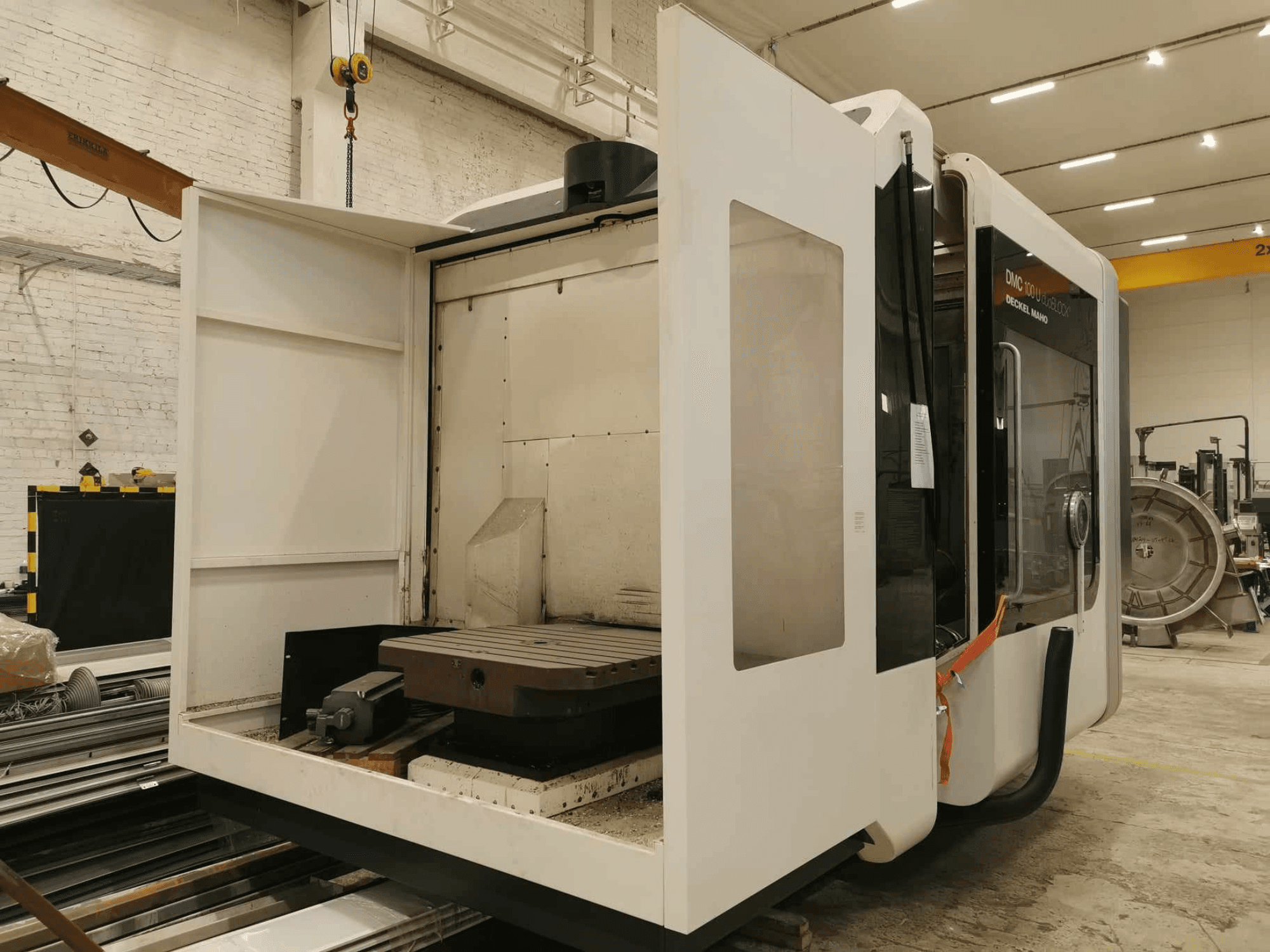 Máquina CNC lineal DMC 100U, vista lateral con la puerta de acceso abierta, mostrando la mesa de trabajo y los componentes internos.
