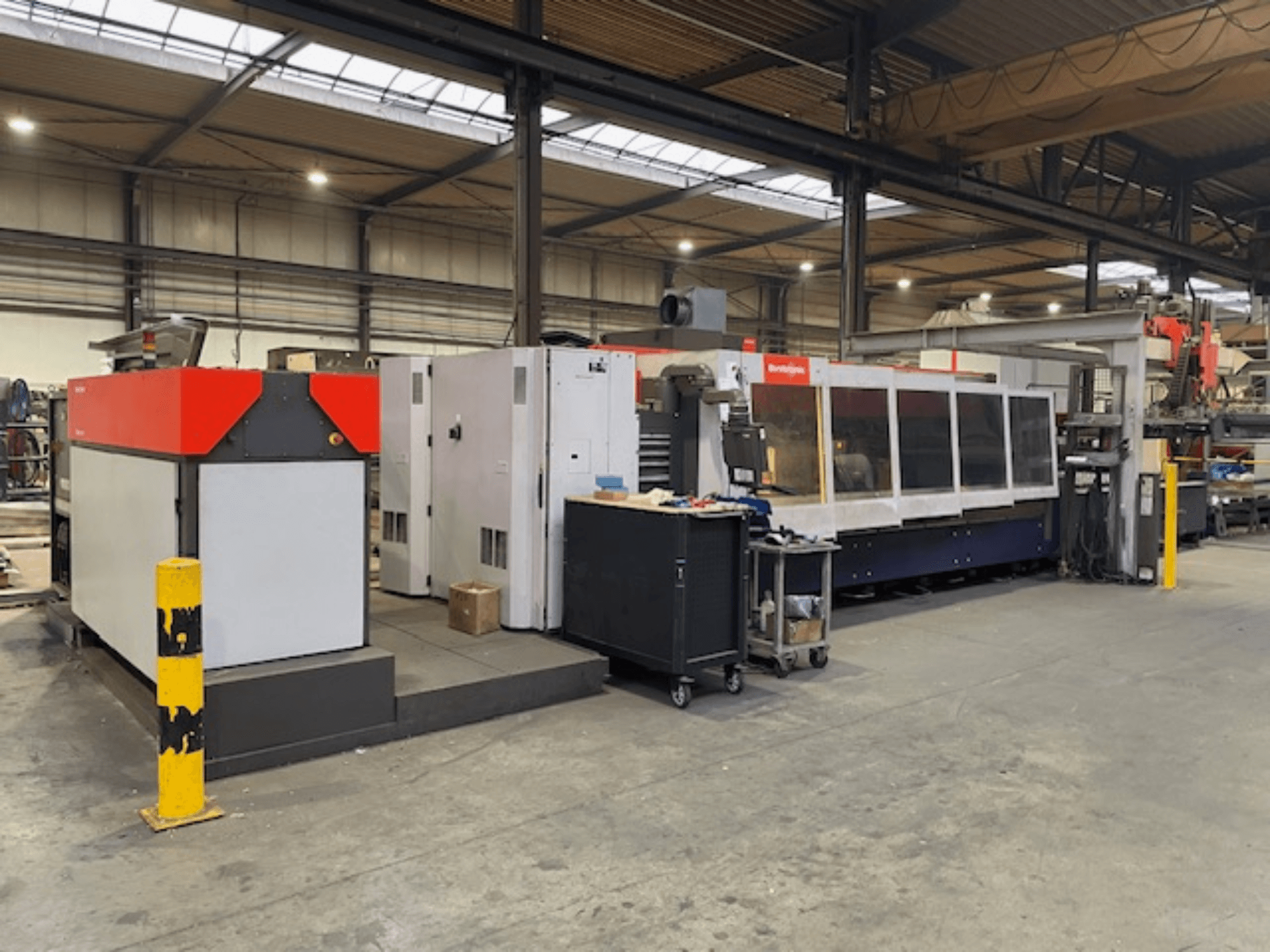 Máquina de corte por láser de CO2 Bystronic BySpeed 3015, vista lateral en un taller, con elementos de diseño distintivos en rojo y gris.