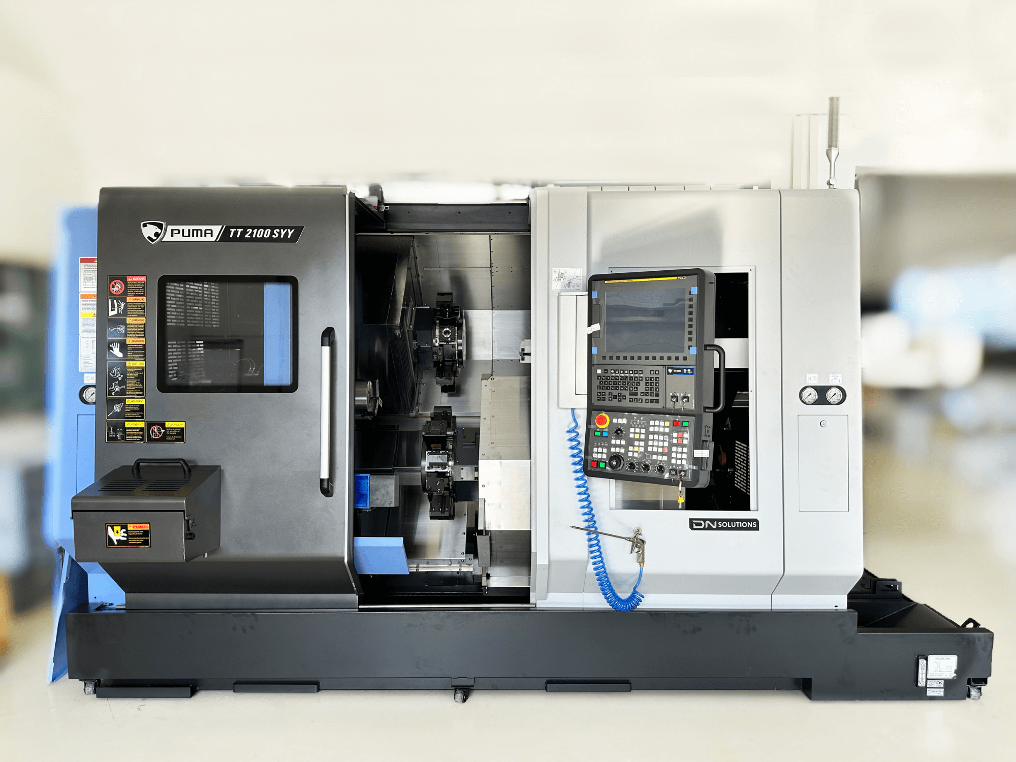 Centro de torneado y fresado DN SOLUTIONS PUMA TT2100SYY vista frontal, con panel de control y componentes interiores visibles.