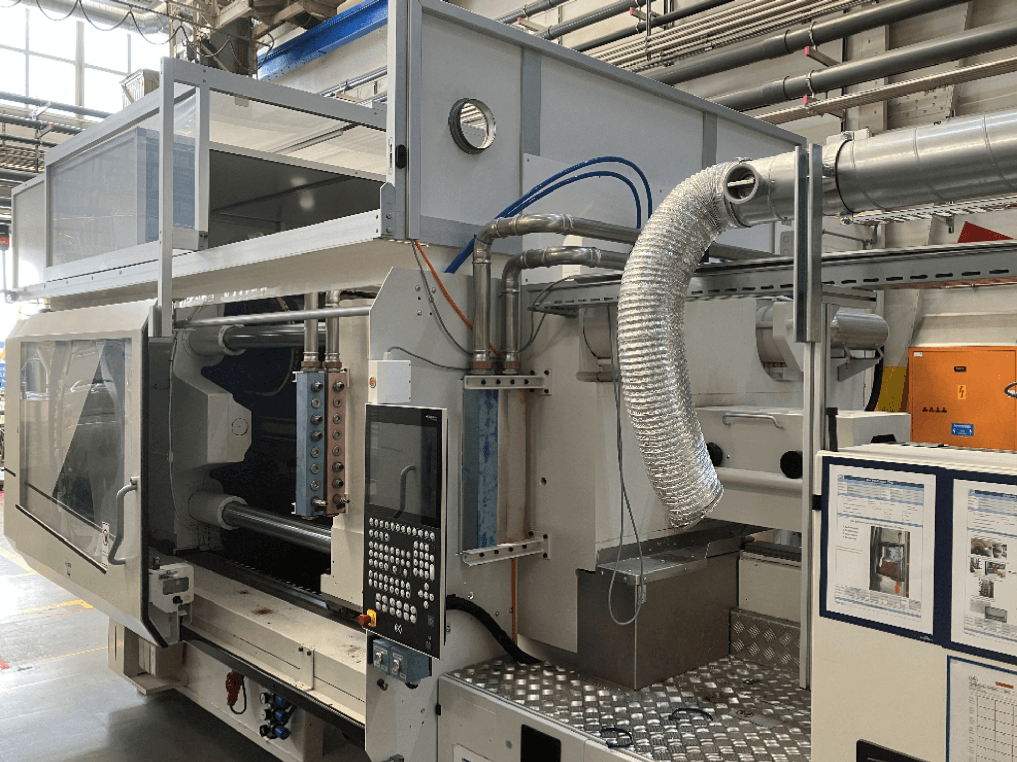 Máquina industrial de la marca X, vista lateral que muestra el panel de control, los conductos y los componentes de la maquinaria en un entorno de fábrica.