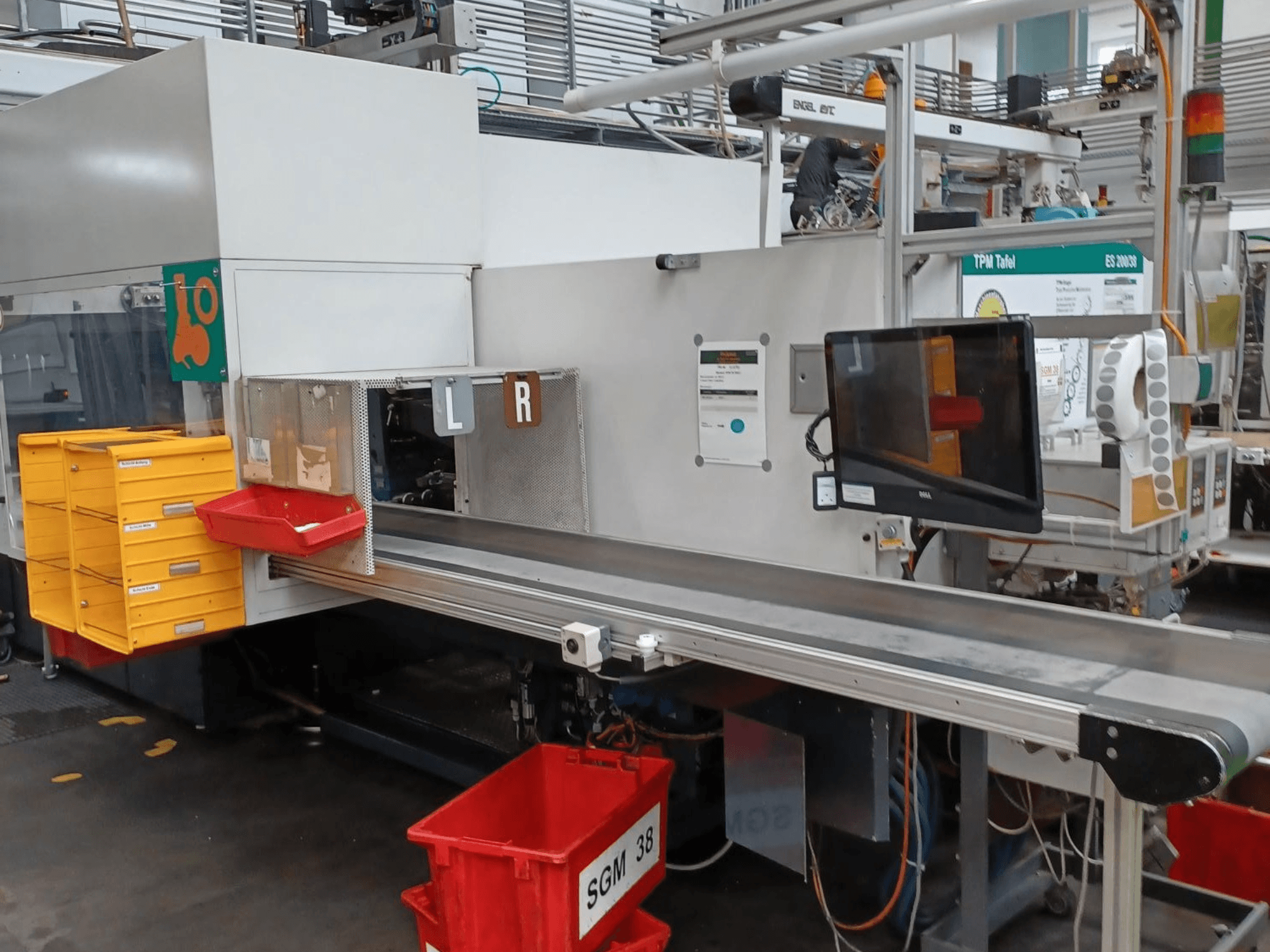 Máquina clasificadora industrial con contenedores amarillos y rojos, vista lateral, con un monitor de control y compartimentos etiquetados para la clasificación.