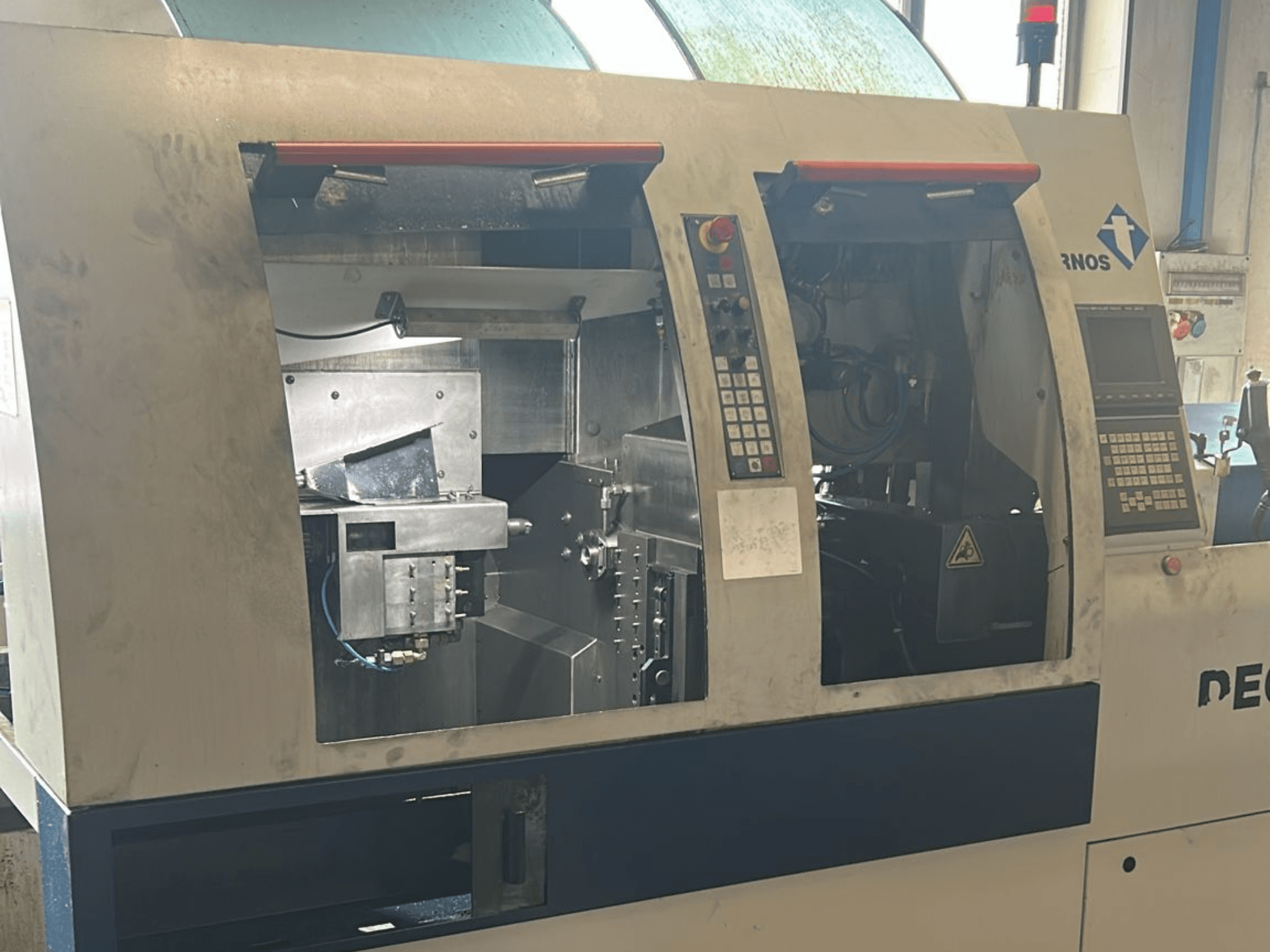 Texto alternativo: Vista frontal de la máquina de torneado de tipo suizo TORNOS Deco 13 b con paneles de control y componentes internos visibles.
