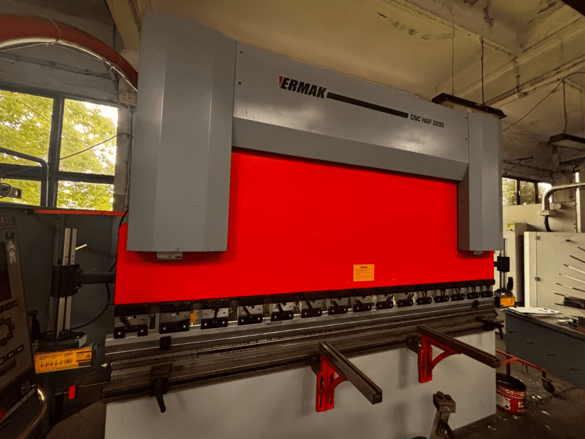 VeriMak CNC HAP 3200 hydraulic press brake, front view, with a bright red bending surface and adjustable clamps visible.