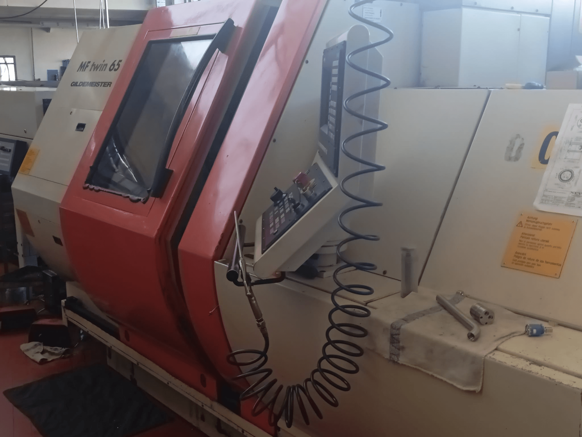 Máquina MF twin 65 Gliedemeister naranja y blanca, vista frontal, con panel de control y herramientas sobre un paño.