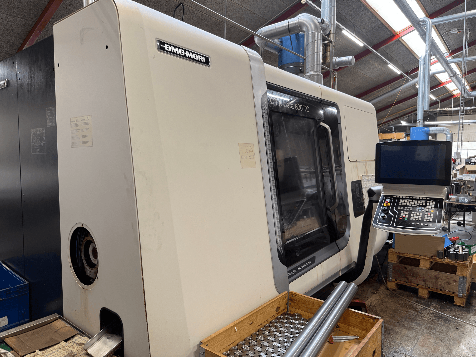 DMM-MORI CTX beta 800 TC machine, front view, with control panel, tools, and metal rods on a wooden pallet.