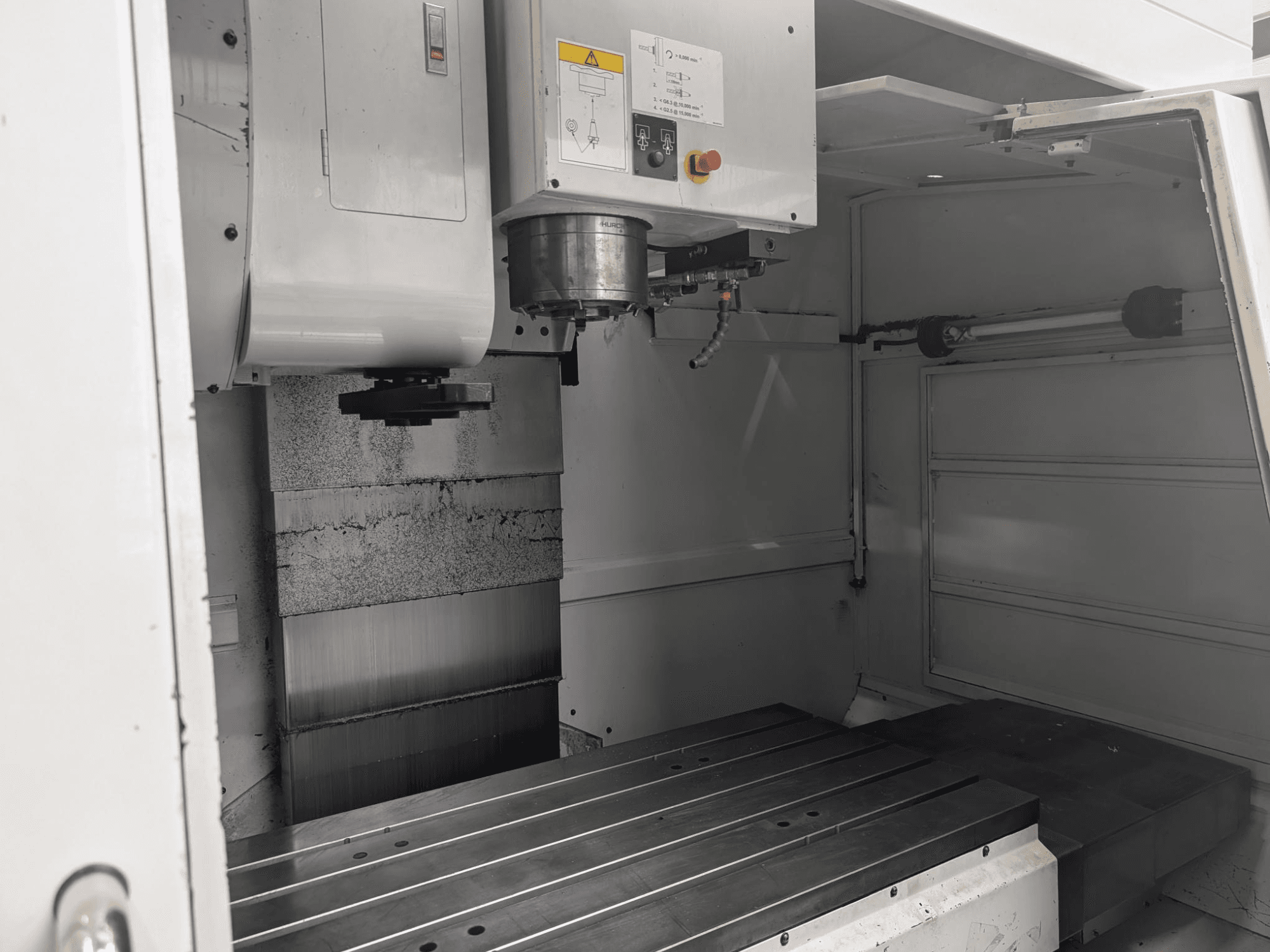 Vista interior de una fresadora CNC con una gran mesa de trabajo metálica y motor de husillo, mostrando los componentes detallados y el panel de control.