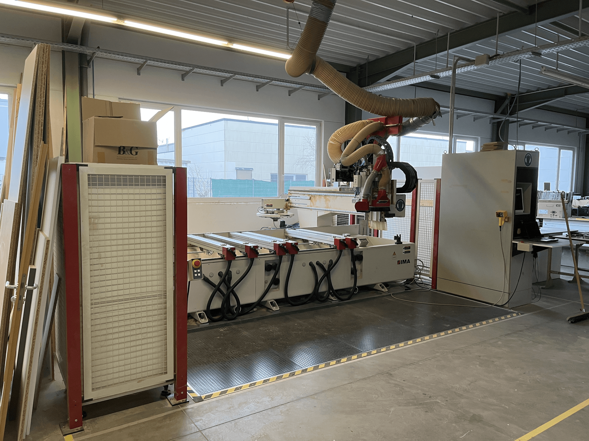 Centro de mecanizado CNC de madera IMA BIMA 410 en taller, vista lateral con panel de control y sistema de extracción de polvo visibles.