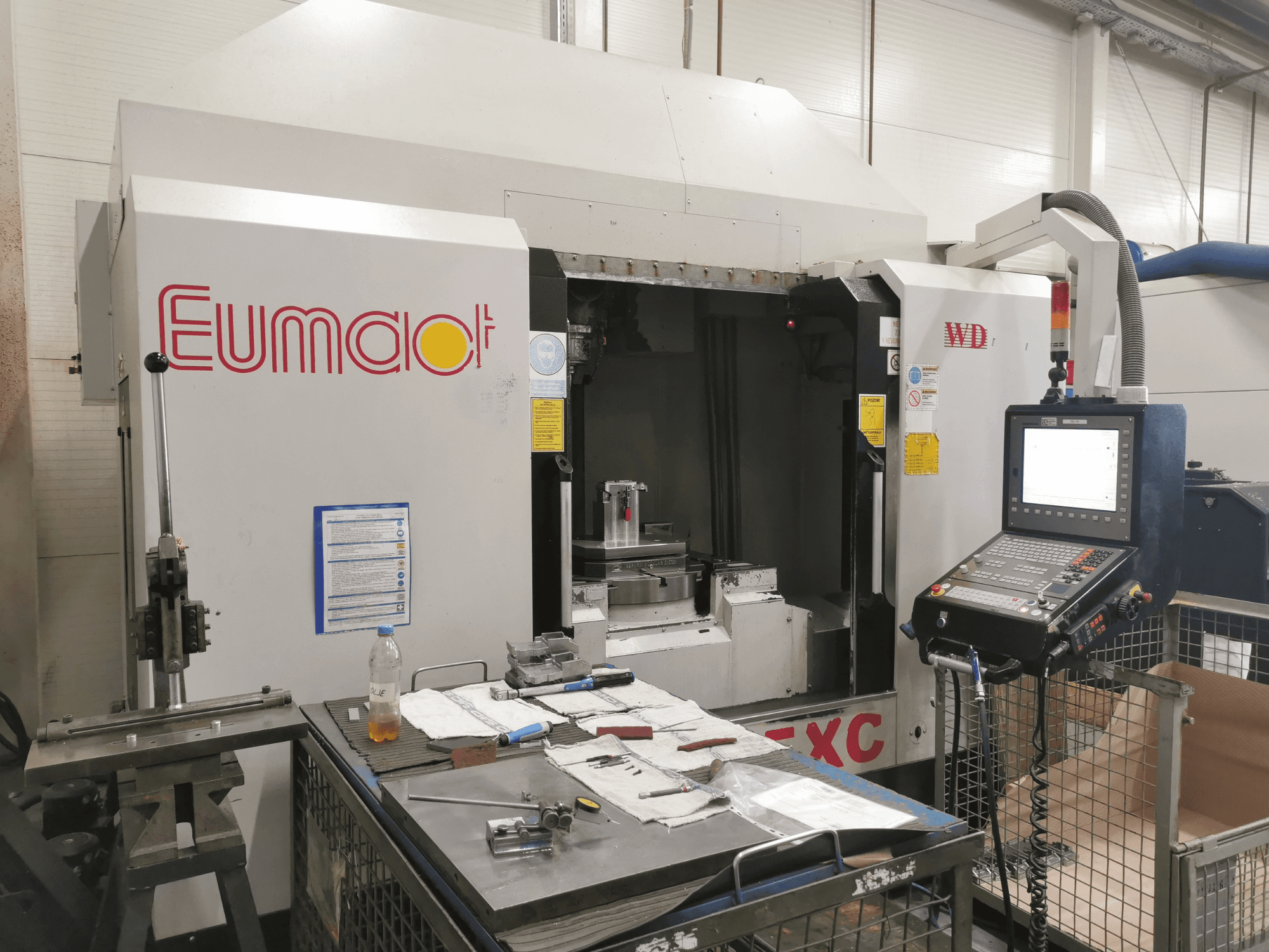 Vista frontal de una máquina CNC Eumdaot con panel de control, herramientas y una superficie de trabajo repleta de componentes y materiales.