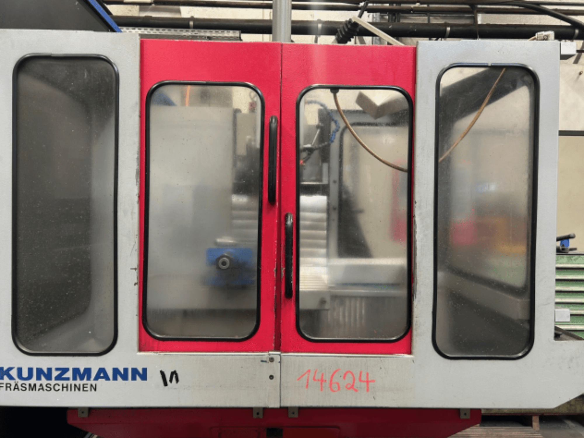 Vista frontal de máquina CNC KUNZMANN, con paneles rojos y grises, con panel de control visible y portaherramientas en el interior.
