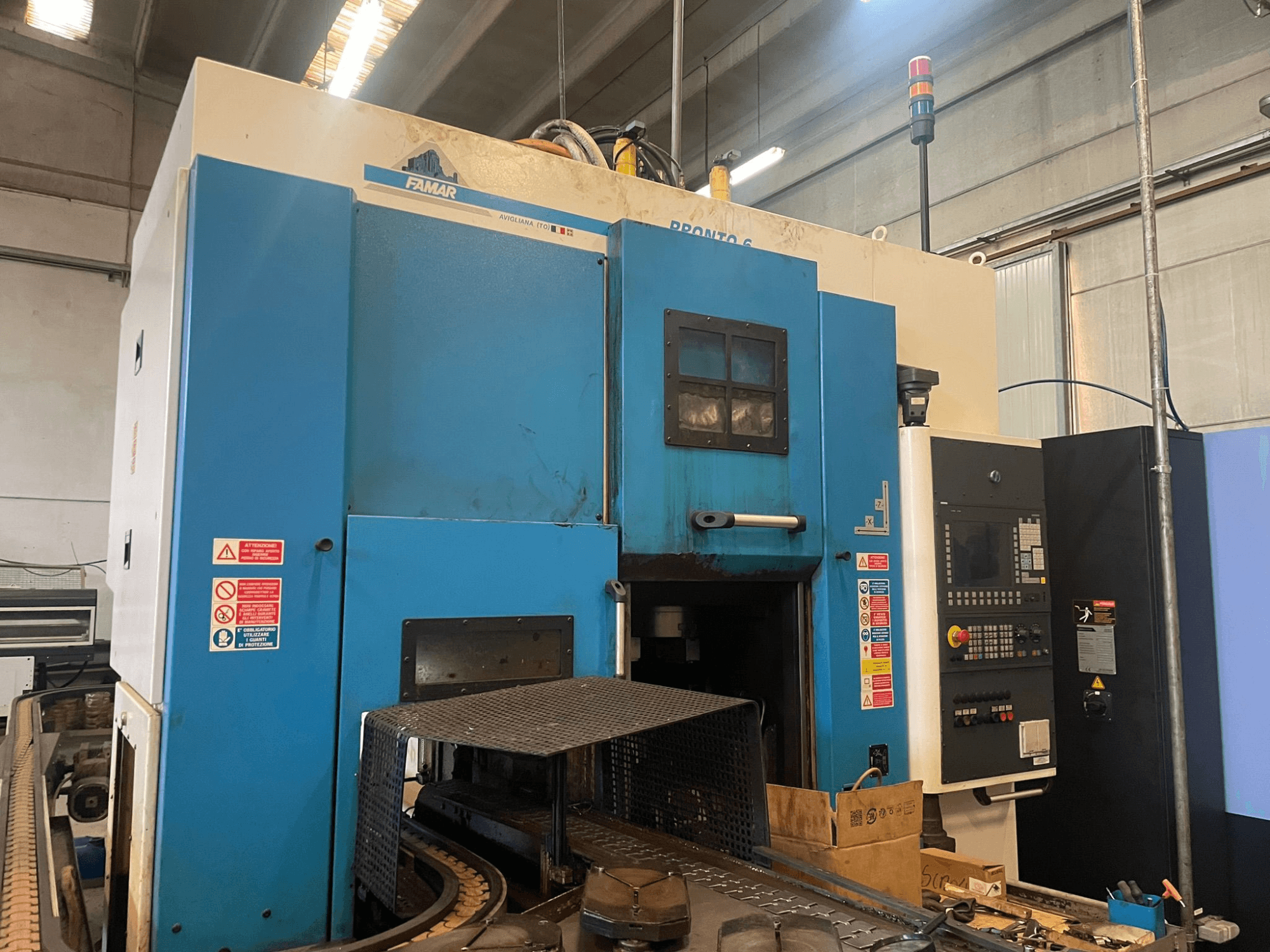 Máquina de torneado vertical Famar Pronto 6 en un taller, vista lateral, mostrando el panel de control, las características operativas y las etiquetas de seguridad.