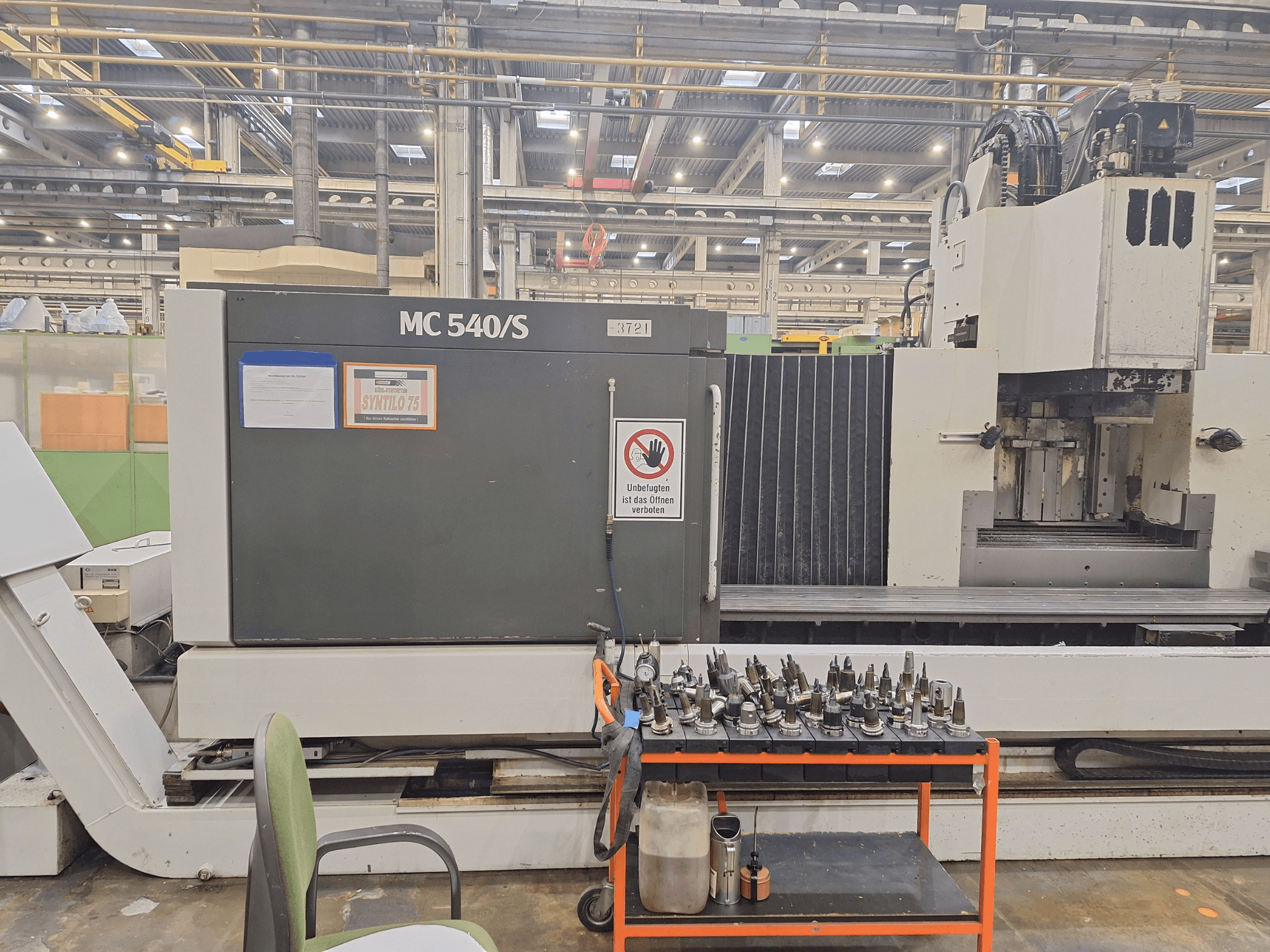 Centro de mecanizado vertical STAMA MC 540S en un taller, vista lateral con portaherramientas en un carro cercano.