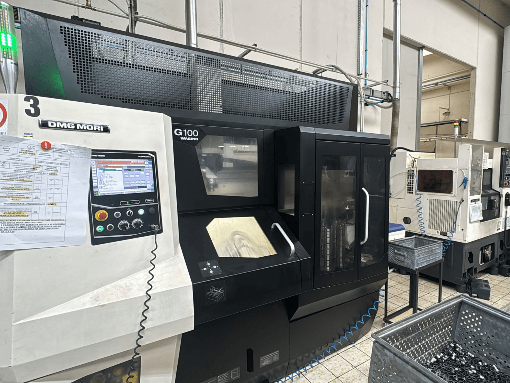 DMG MORI G100 machine in a factory, front view, featuring a digital control panel and nearby tool storage bins.