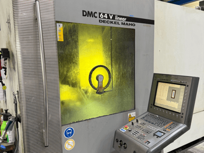 DMC 64 V lineal de Deckel Maho, vista frontal de la máquina con panel de control y ventana tintada en amarillo que muestra los mecanismos interiores.