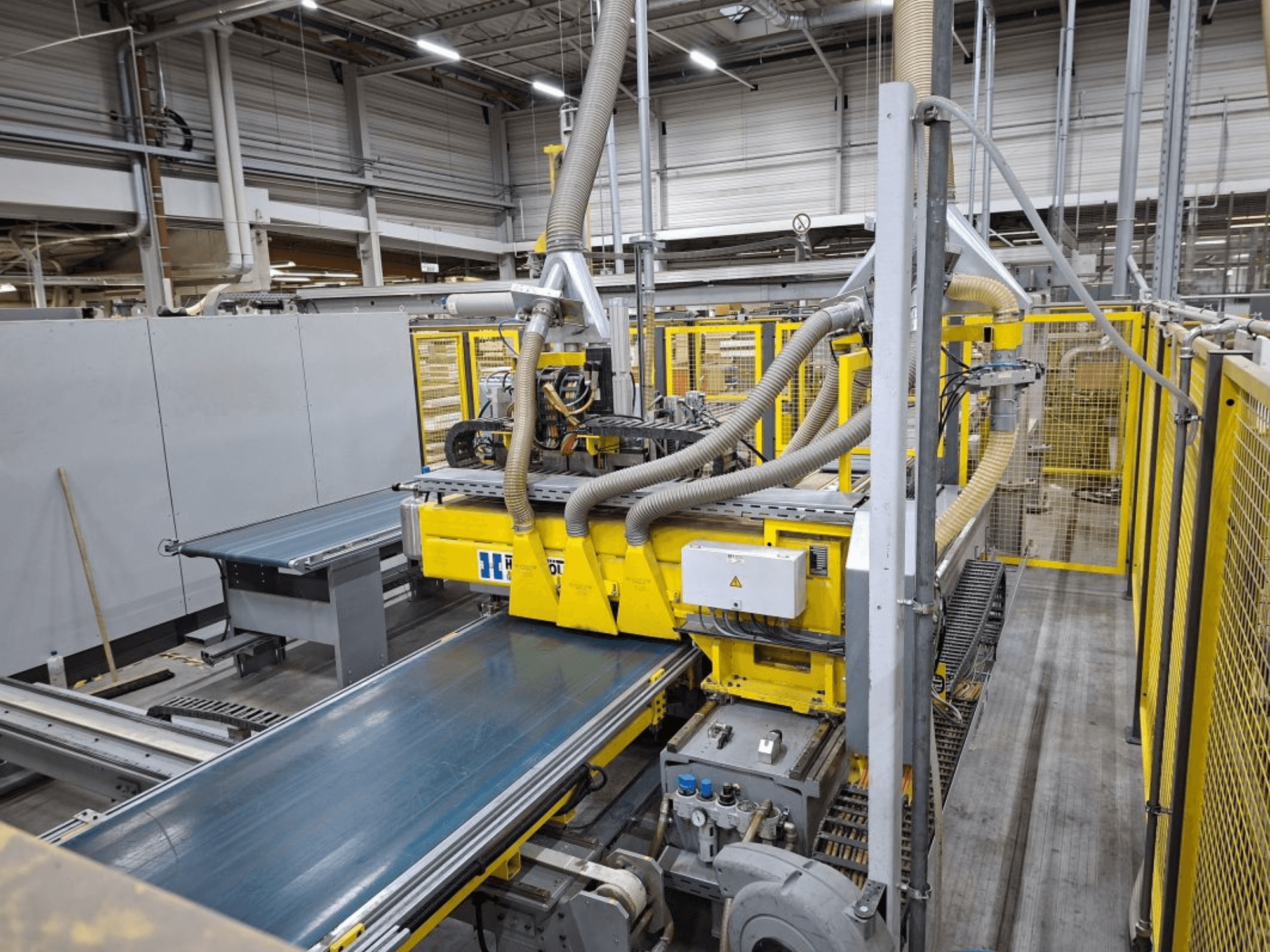 Sistema de transporte industrial desde una vista lateral, con maquinaria amarilla, panel de control y accesorios de manguera para la fabricación.