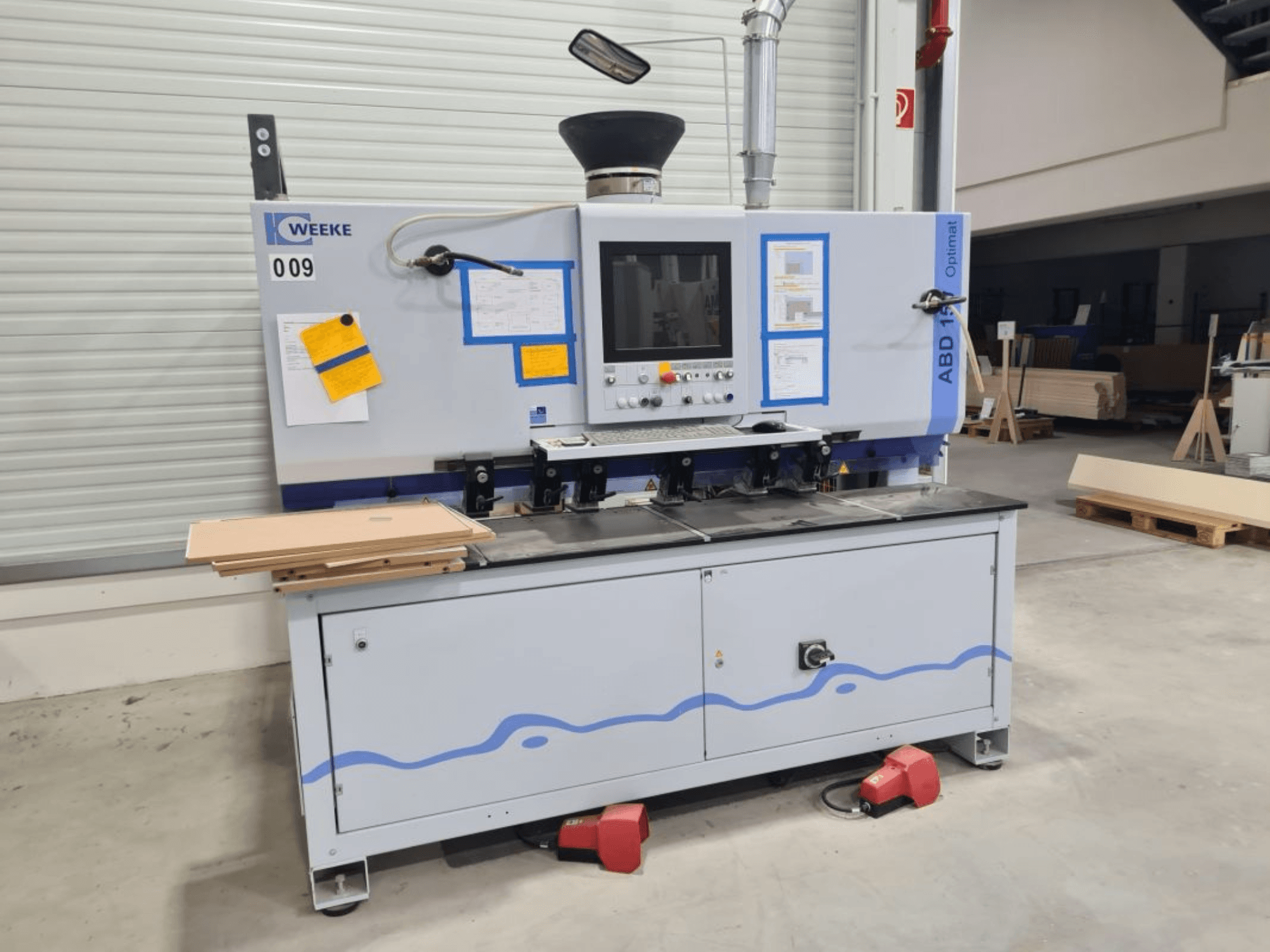 Taladradora multihusillo HOMAG WEEKE OPTIMAT ABD150, vista frontal, mostrando controles y paneles de madera apilados.