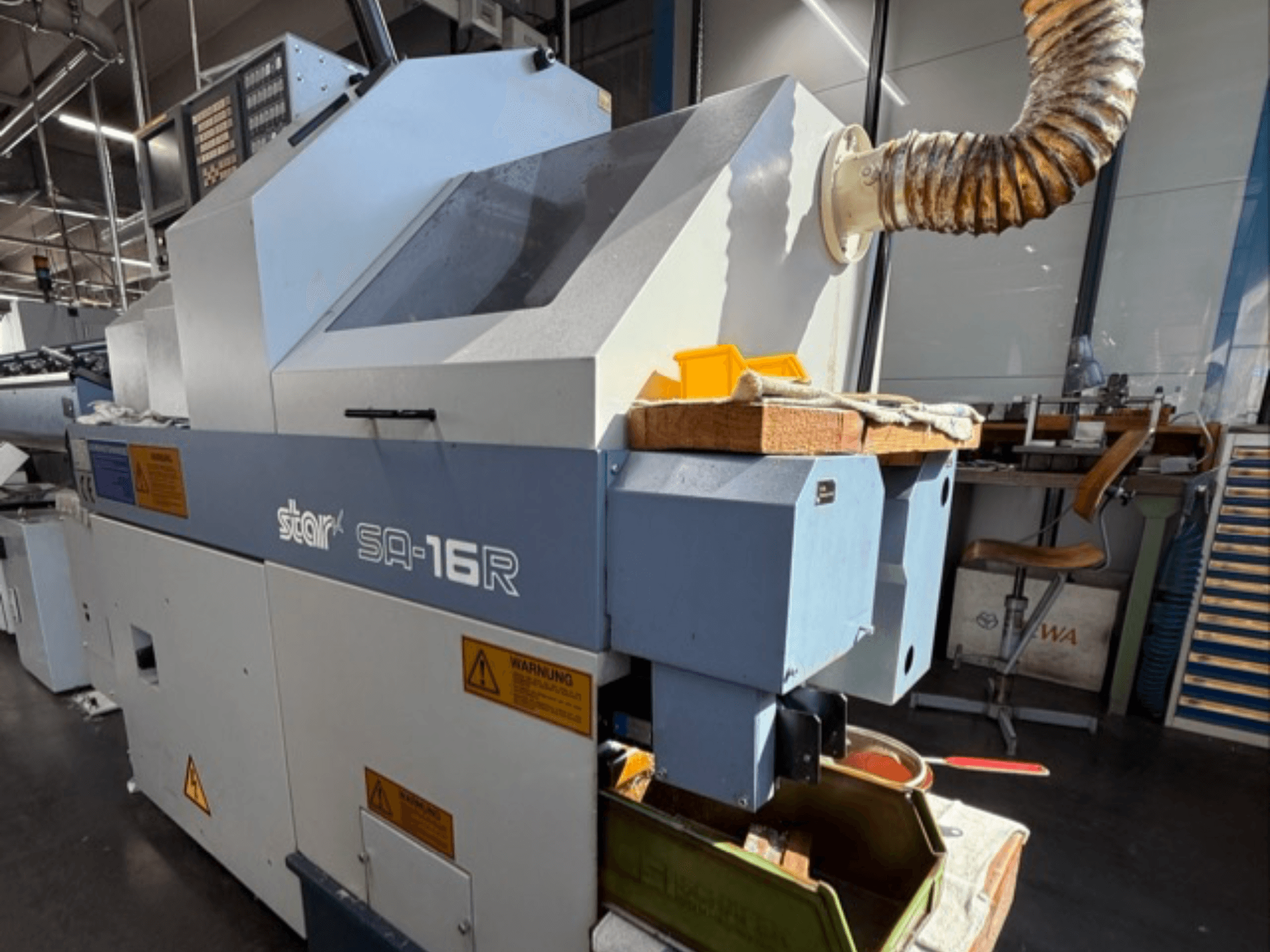 Máquina Stark SA-16R vista de frente, con escape cónico y espacio de trabajo con herramientas y etiquetas de advertencia amarillas.