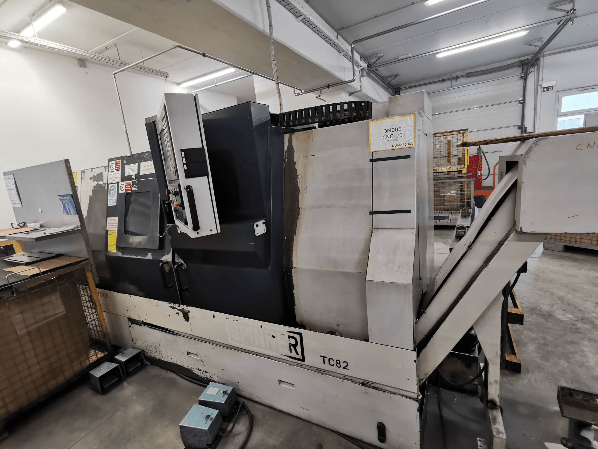 Máquina CNC, marca Spinner, modelo TC82, vista lateral que muestra el panel de control y la tolva de retirada de chatarra en un taller.