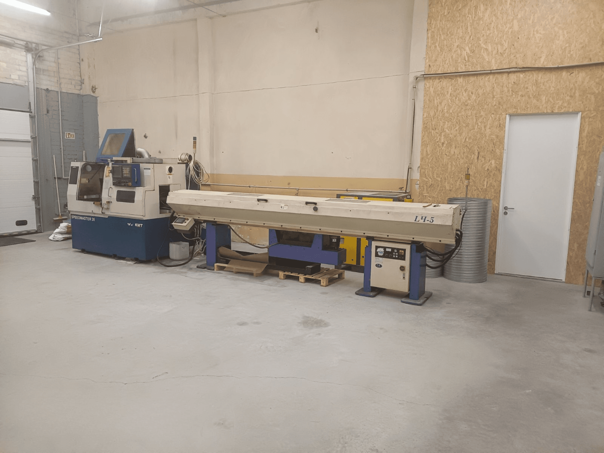 Taller industrial con máquina KMT Speedmaster 34 y L4.5, vista de frente, con controles y maquinaria visibles.