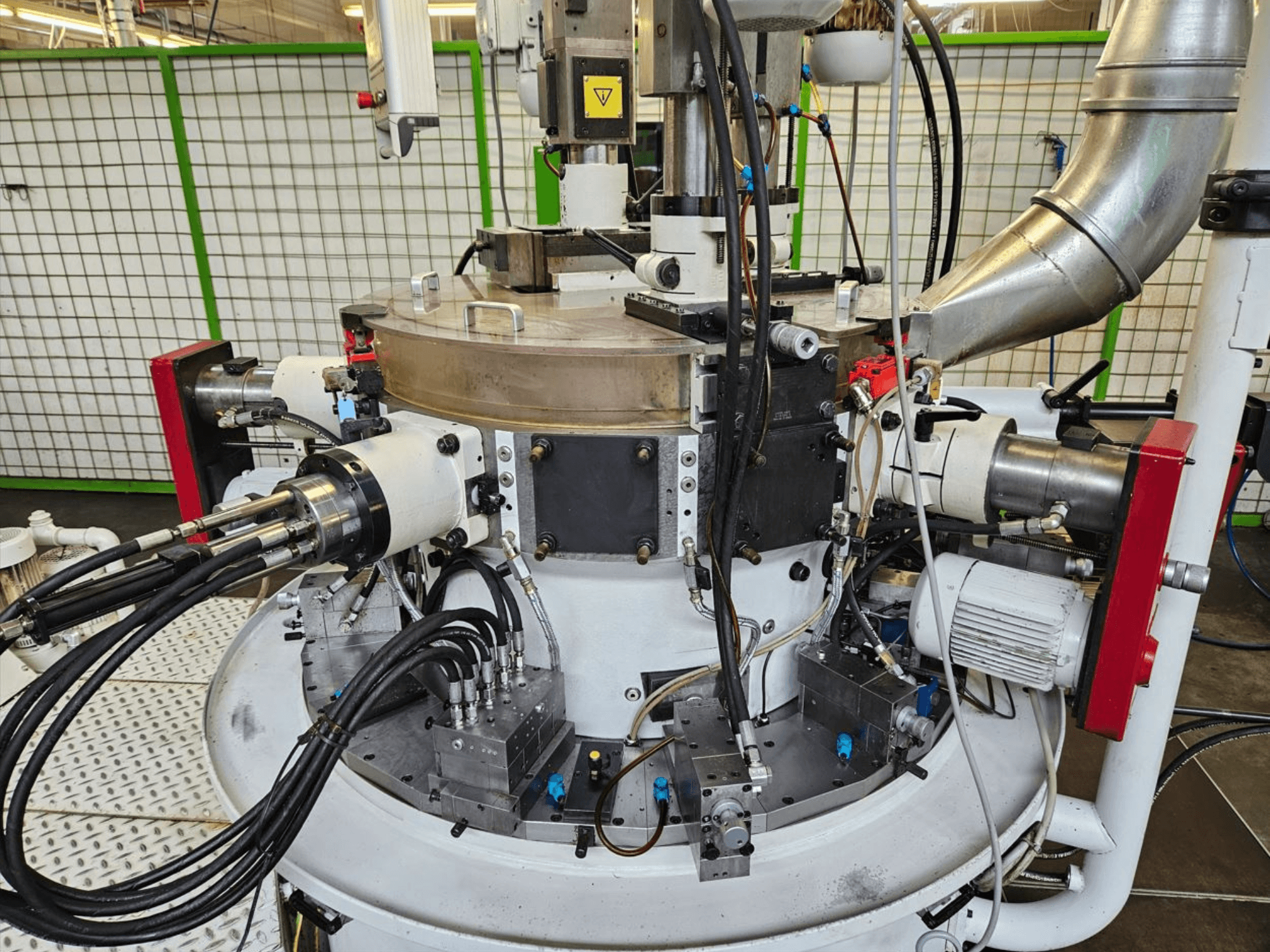 Primer plano de una máquina industrial con mangueras hidráulicas, componentes metálicos y una base giratoria. No se ve ninguna marca.