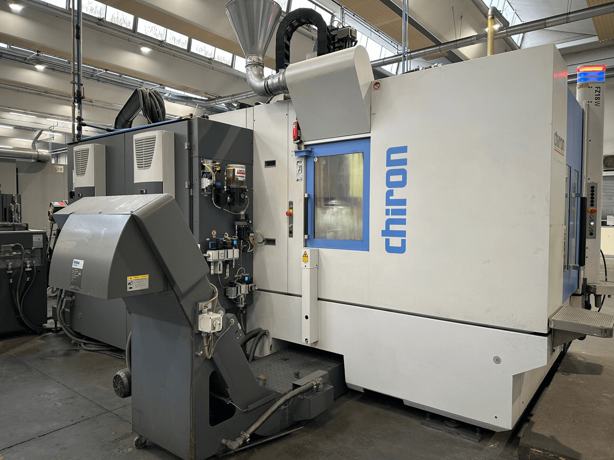 Máquina CNC Chiron en gris y blanco, vista frontal, con controles, tuberías y una campana de extracción de polvo.