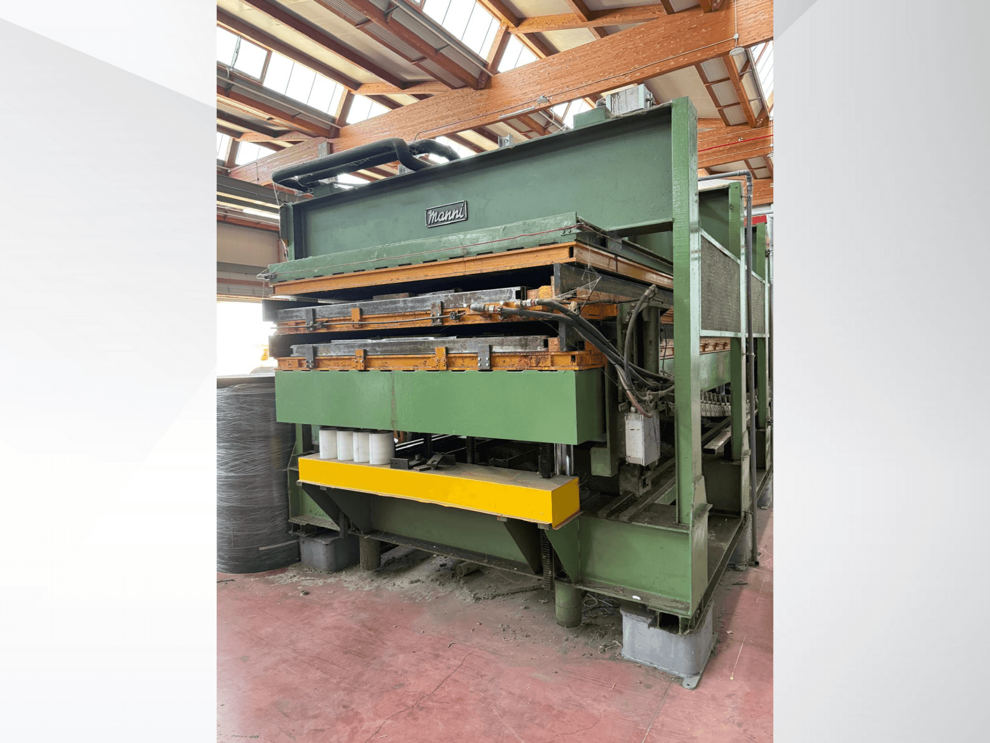 Prensa hidráulica Manni, vista lateral, con cuerpo metálico verde, base amarilla y múltiples conductos hidráulicos visibles.