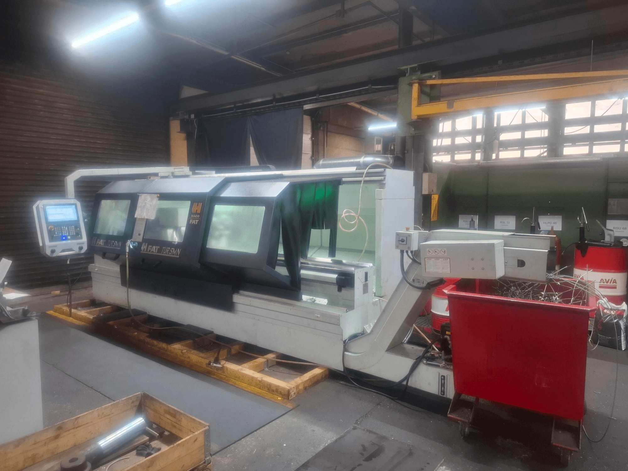 Vista frontal de una máquina CNC FAT Tursan con panel de control, colocada sobre palés de madera en un taller.