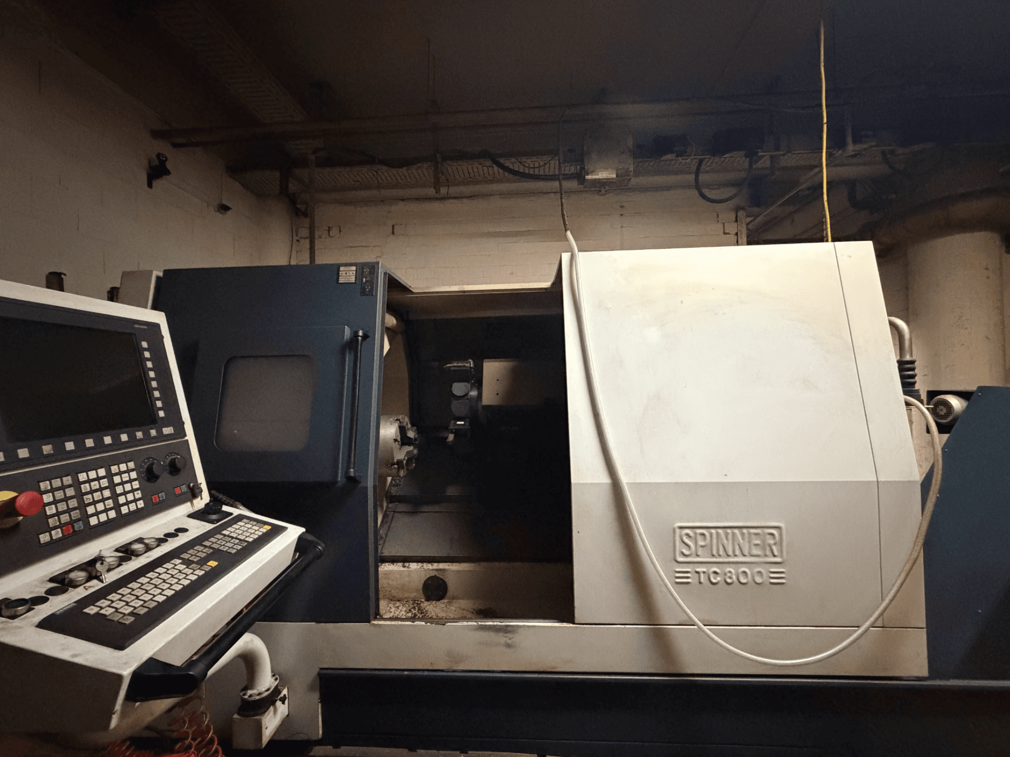 Máquina de torneado horizontal SPINNER TC800, vista frontal con el panel de control visible y el interior de la máquina ligeramente expuesto.