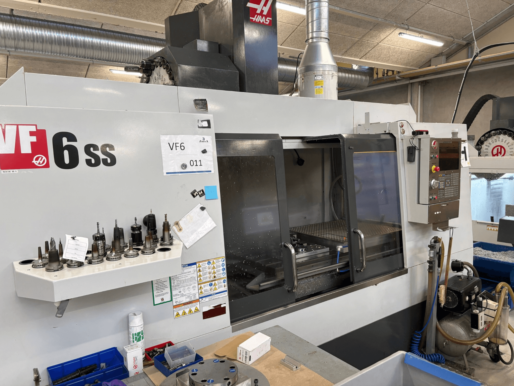 Fresadora CNC Haas VF-6 SS, vista frontal. Incluye varias herramientas, panel de control y espacio de trabajo interno visible.