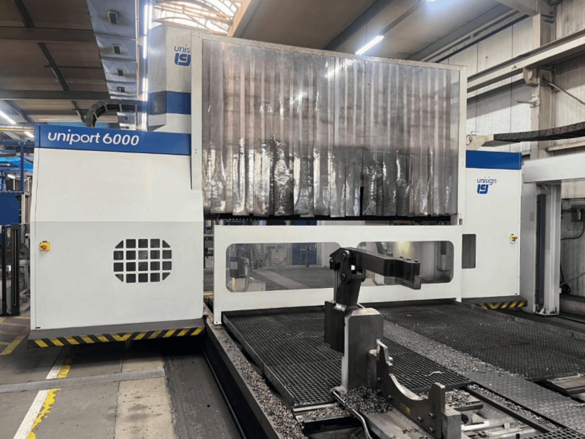 Fresadora de pórtico Unisign uniport 6000, vista frontal, mostrando la estructura de la máquina y la zona de corte con virutas de metal.