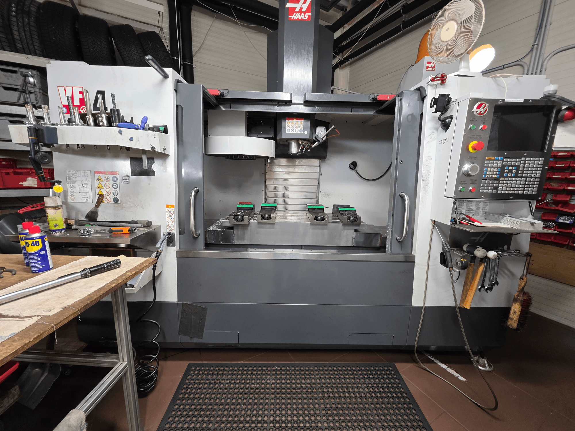 Vista frontal de la fresadora CNC Haas VF-4 en un taller, con herramientas, una interfaz de ordenador y dos piezas sobre la mesa.