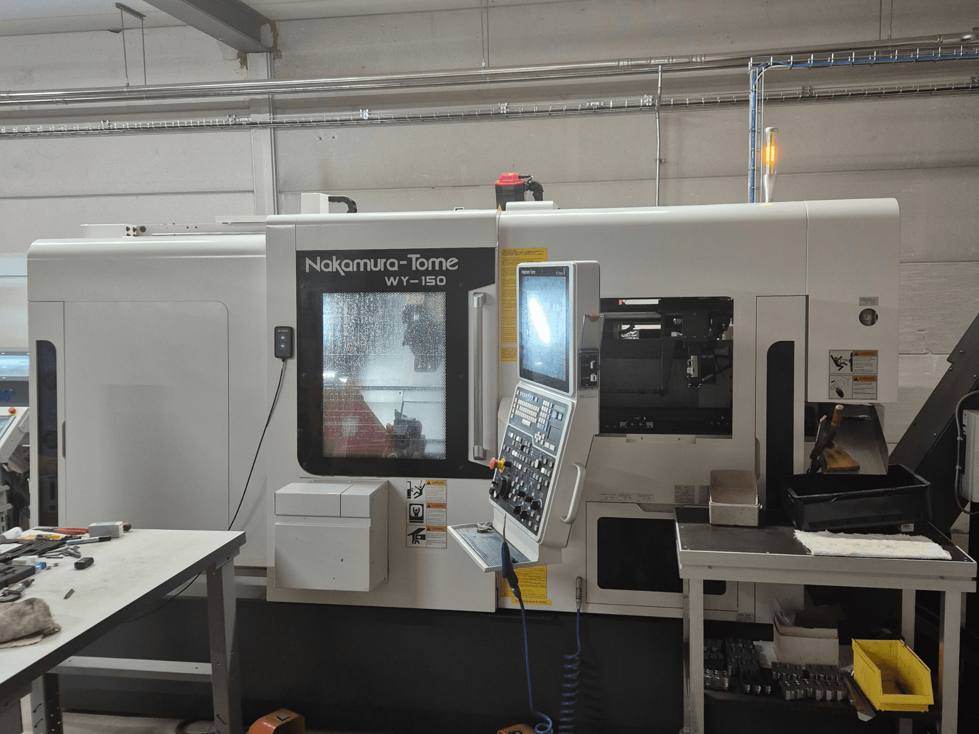 Torno CNC WY-150 de Nakamura-Tome en vista lateral, con panel de control, ventana transparente y área de trabajo visible.