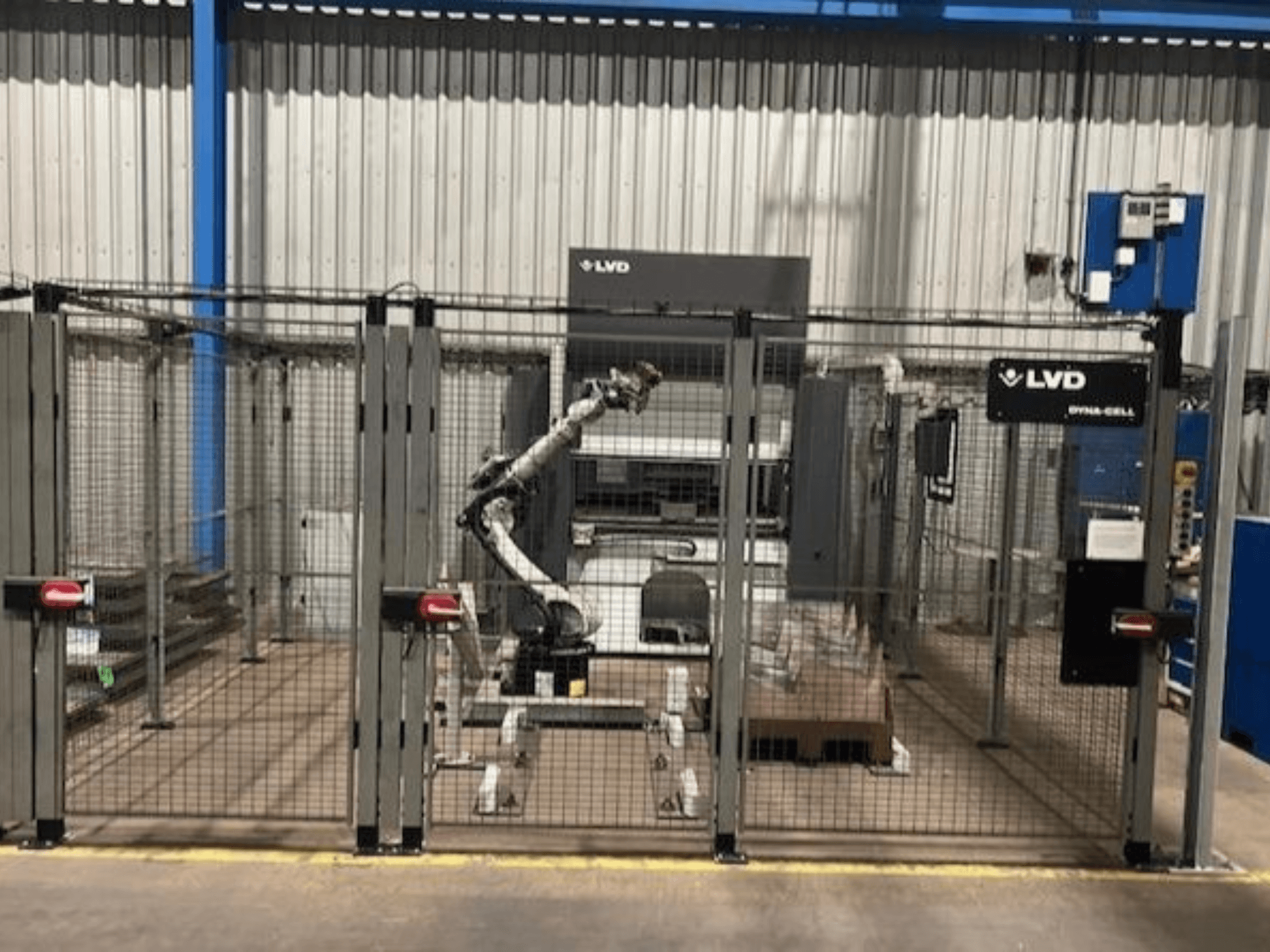 Estación de trabajo robótica LVD Dyna-Cell en un recinto vallado, vista frontal, con brazo robótico y panel de control.