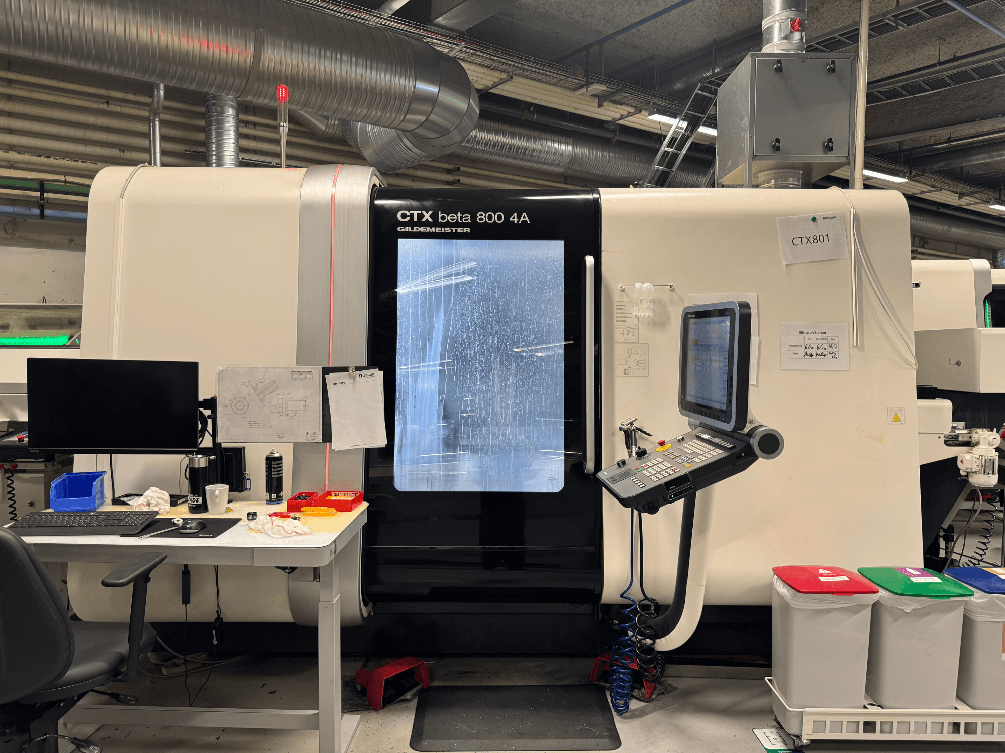 Máquina CTX beta 800 4A con panel de control y monitor, vista lateral, en un taller con configuración de oficina y cubos de basura de colores.