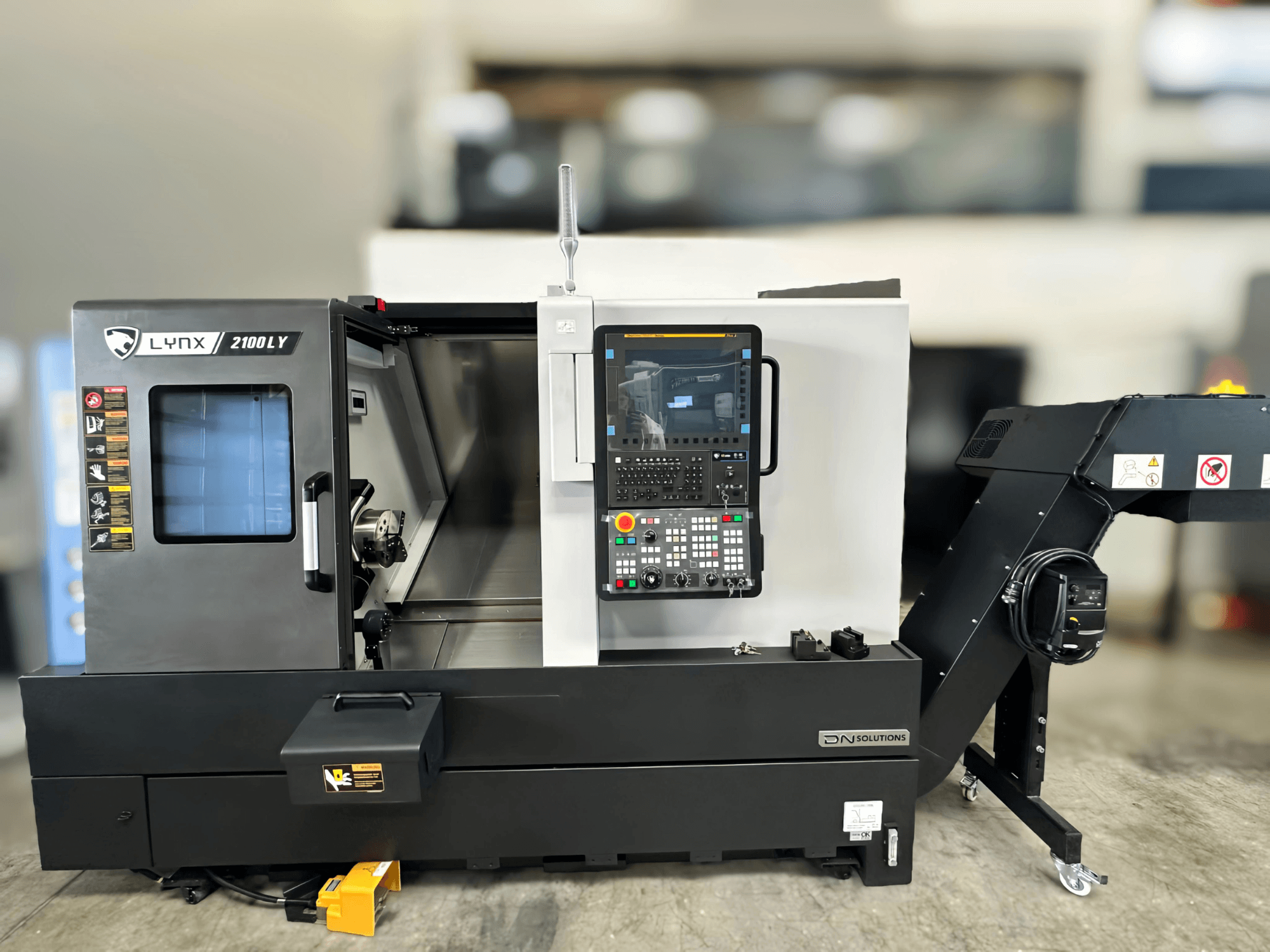 Máquina de torneado horizontal DN SOLUTIONS LYNX 2100LYB, vista frontal, con panel de control y puerta abierta que revela el interior.