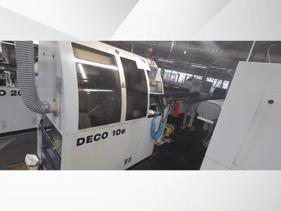Máquina DECO 10e en un taller; vista lateral que muestra el panel de control y la manguera de ventilación, con maquinaria borrosa al fondo.