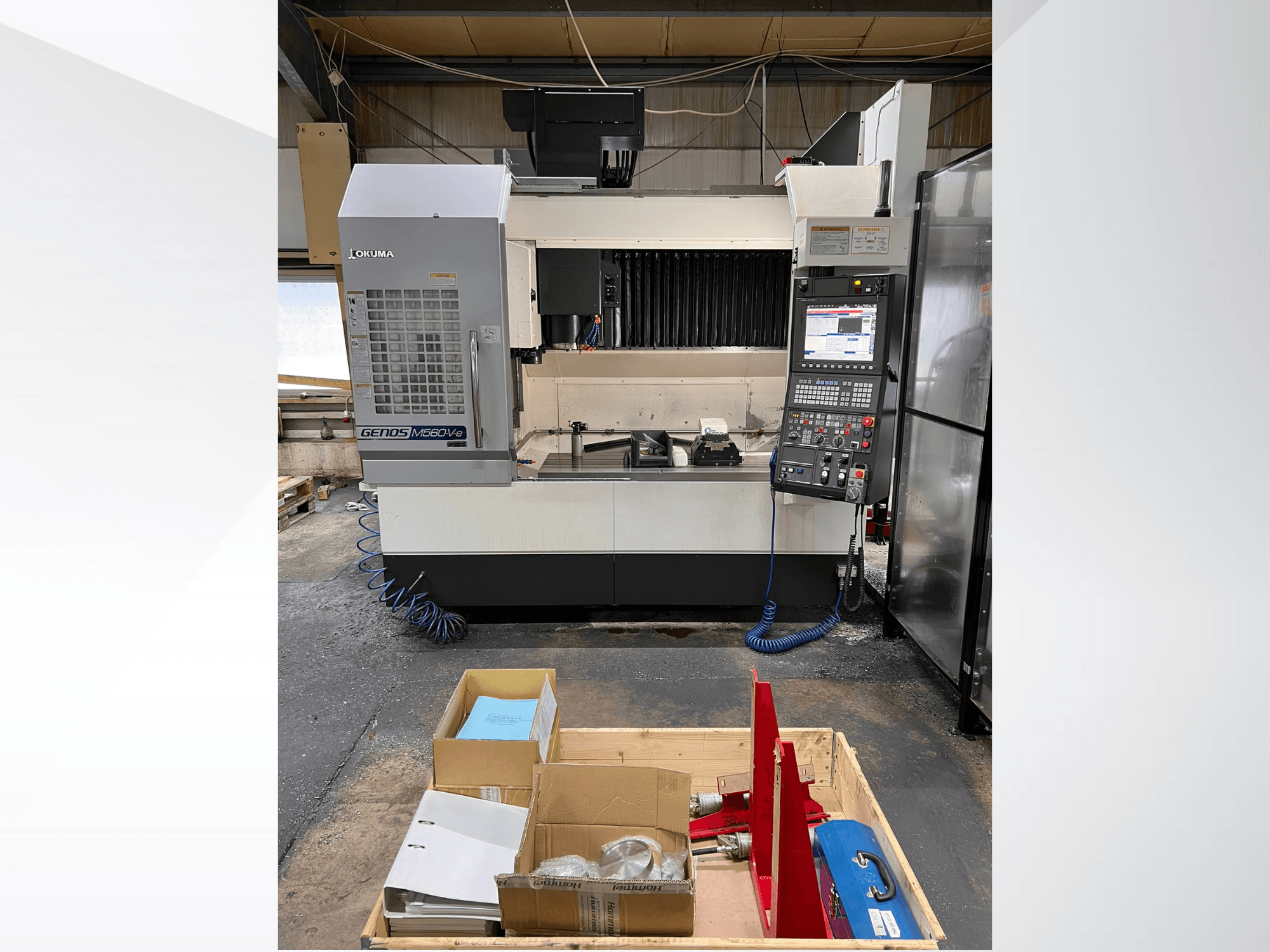 Centro de mecanizado vertical Okuma GENOS M460V-5, vista frontal, con el panel de control visible y las herramientas sobre la mesa de trabajo.