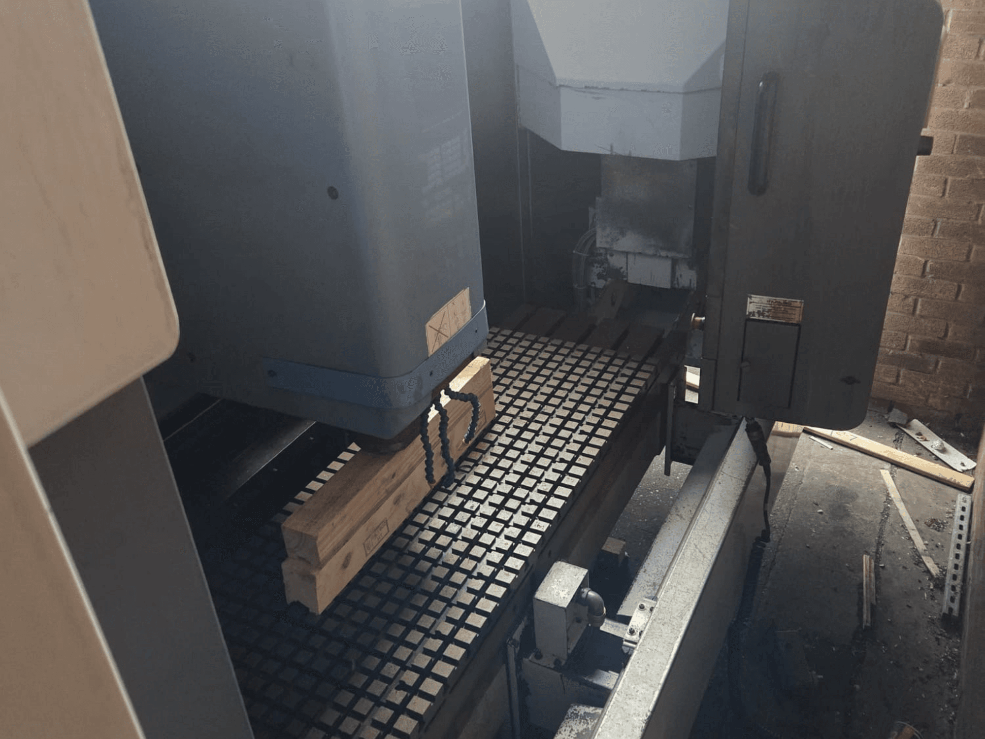 Vista frontal de máquina CNC con tablones de madera sobre una mesa de rejilla, mostrando herramientas y controles en el lateral.