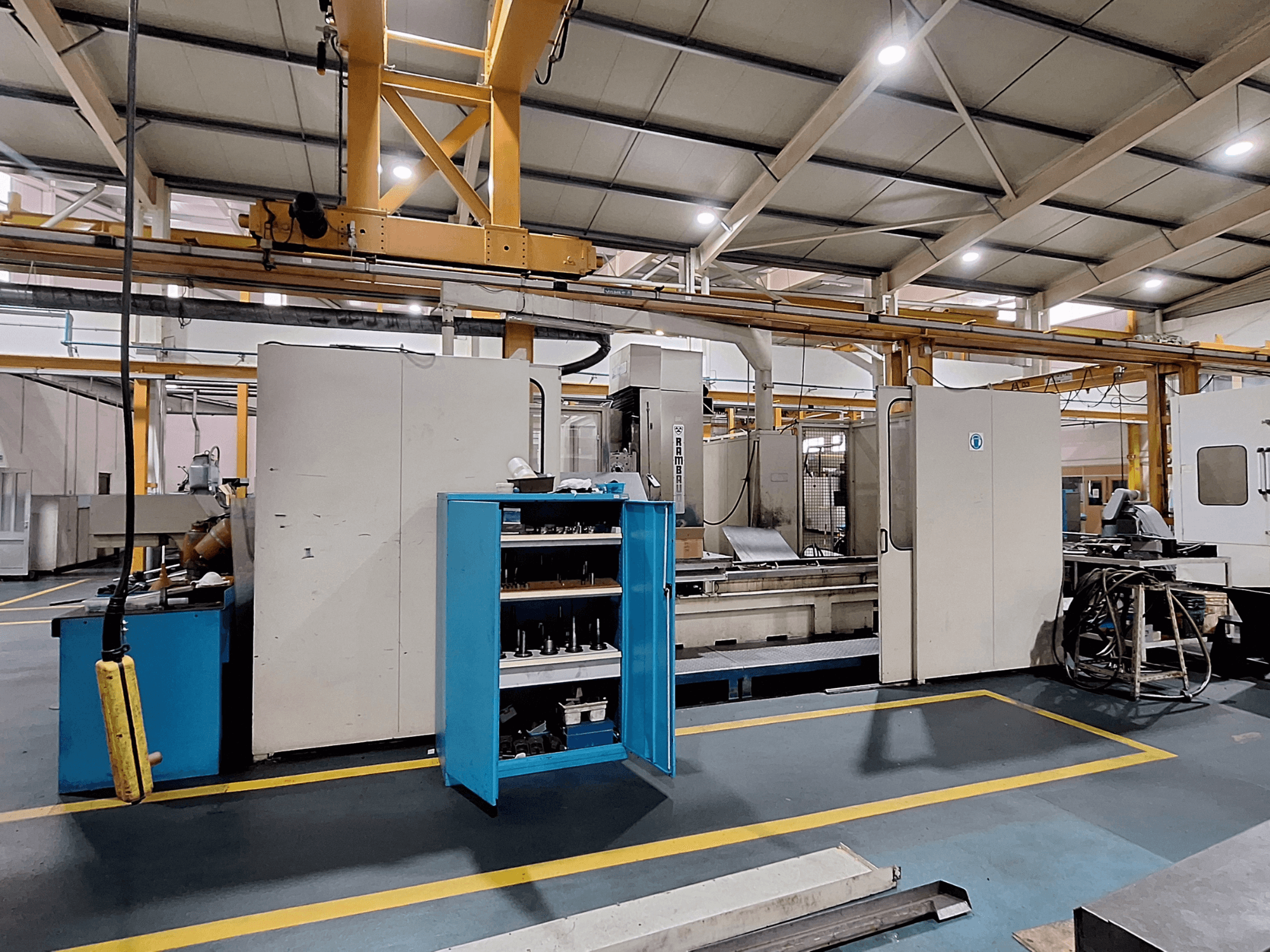 Fresadora de pórtico Rambaudi RX 1250, vista frontal con almacenamiento de herramientas, en un amplio espacio de trabajo industrial.